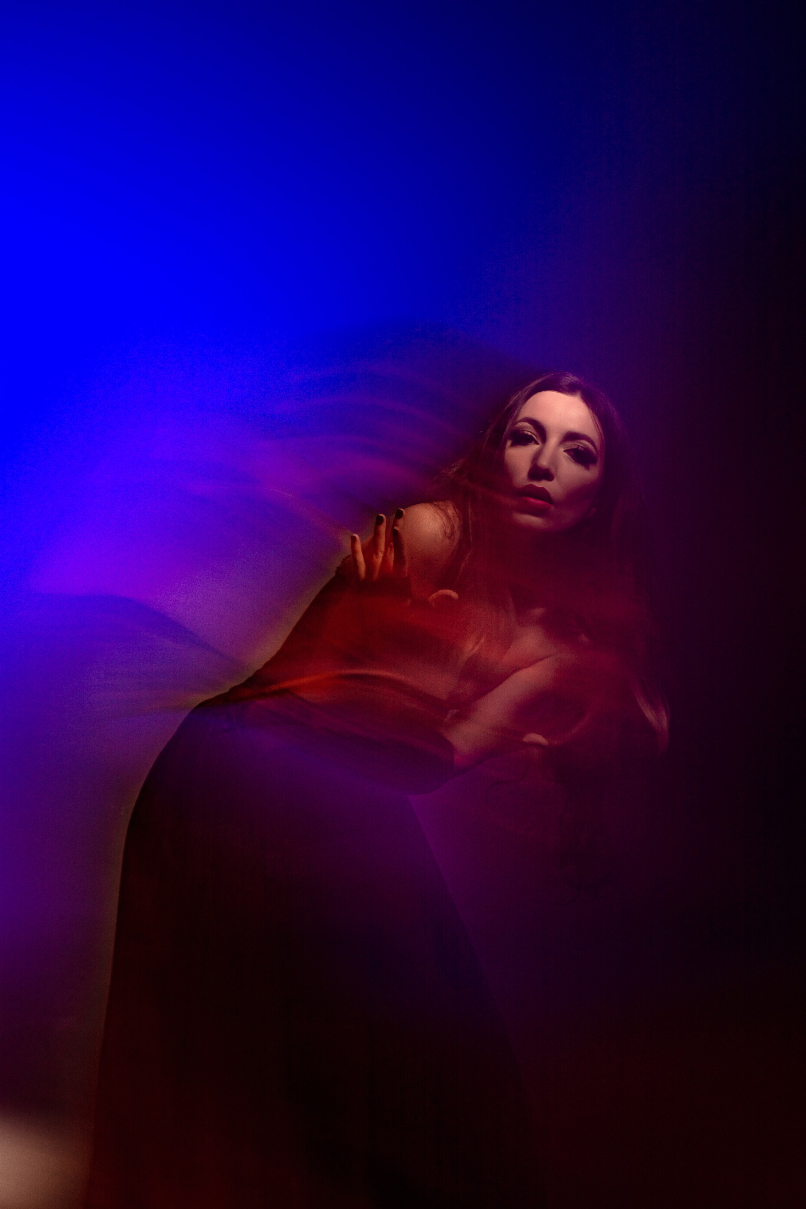 Магия цветов и света: девушка, окруженная красным, синим, бирюзовым и розовым светом, создает неповторимое визуальное шоу в технике смешанного света