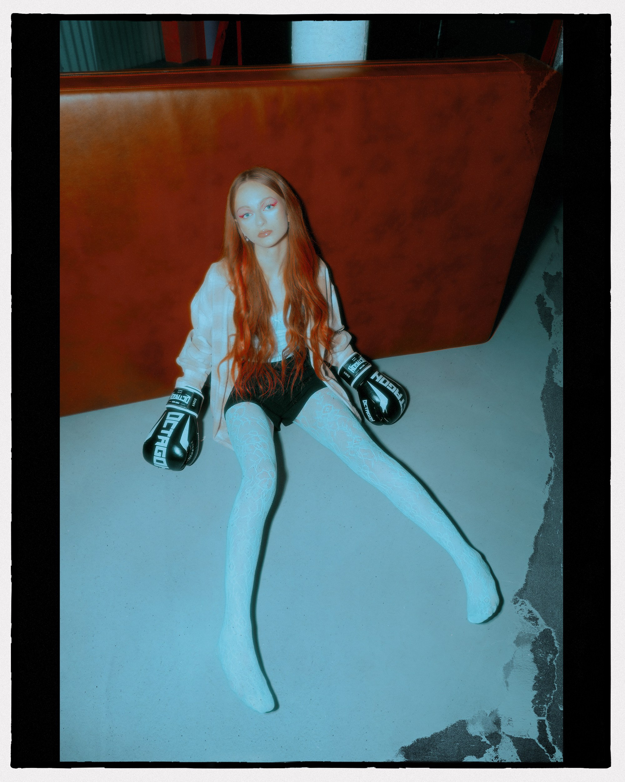 Фэшн фотография для журналов. Рыжая девушка в боксёрских перчатка лежит возле кожаного дивана