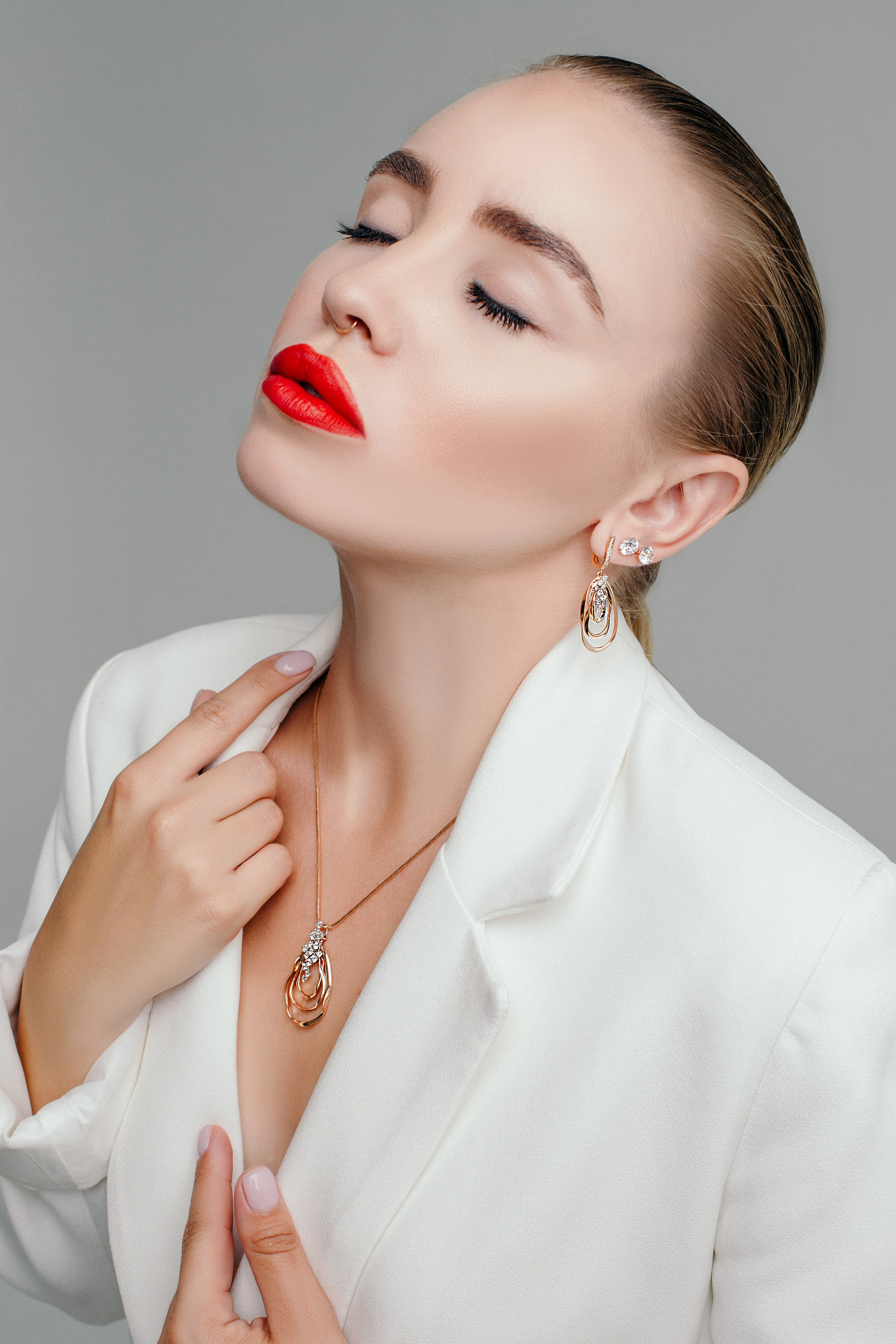 красная помада на губах у девушки в белом пиджаке и в крупных ювелирных украшениях из золота 585 пробы