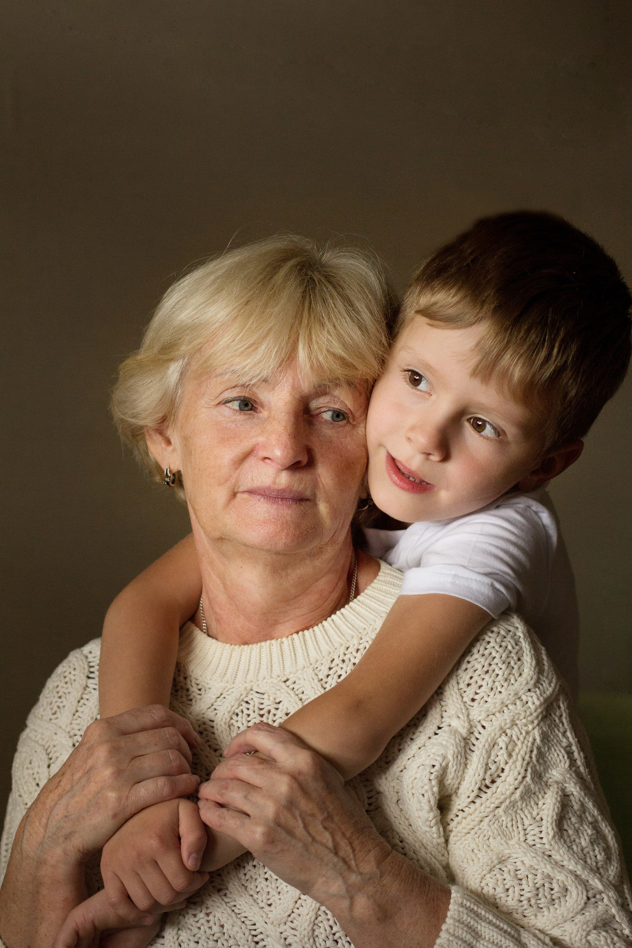 Пятилетний мальчик обнимает бабушку со спины сидя у окна.