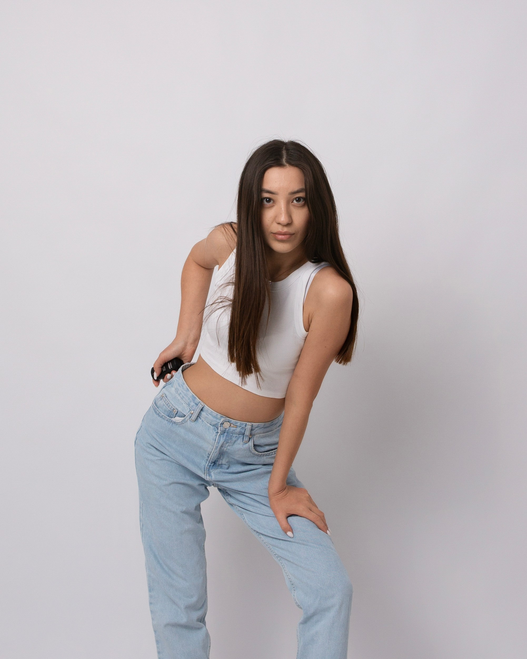 Шатенка в белом топе и голубых джинсах с пультом в руках управляет процессом съемки  в фотостудии 