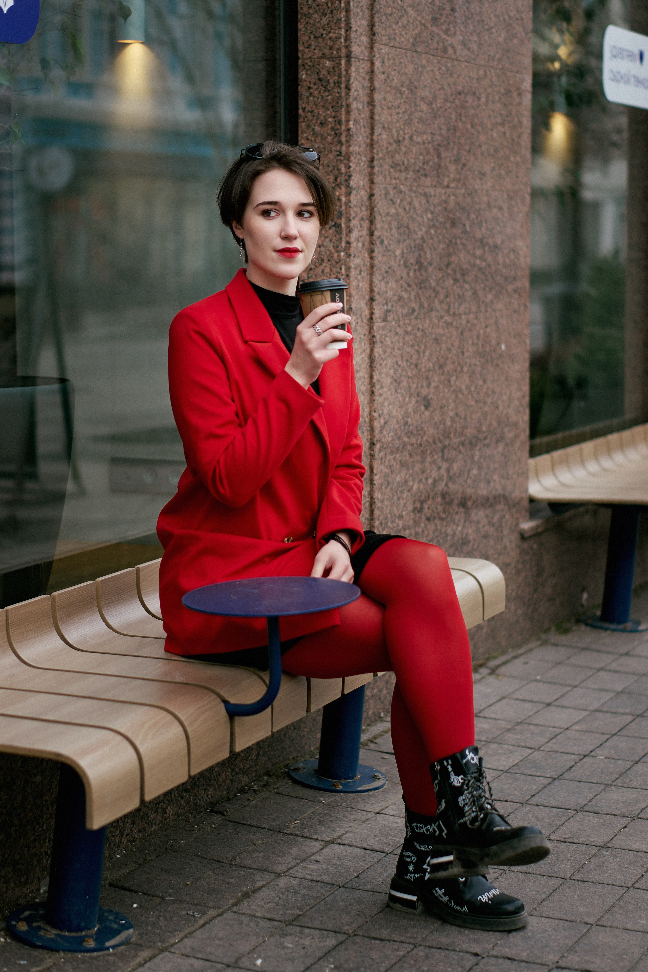 Девушка в красном пиджаке сидит у кафе