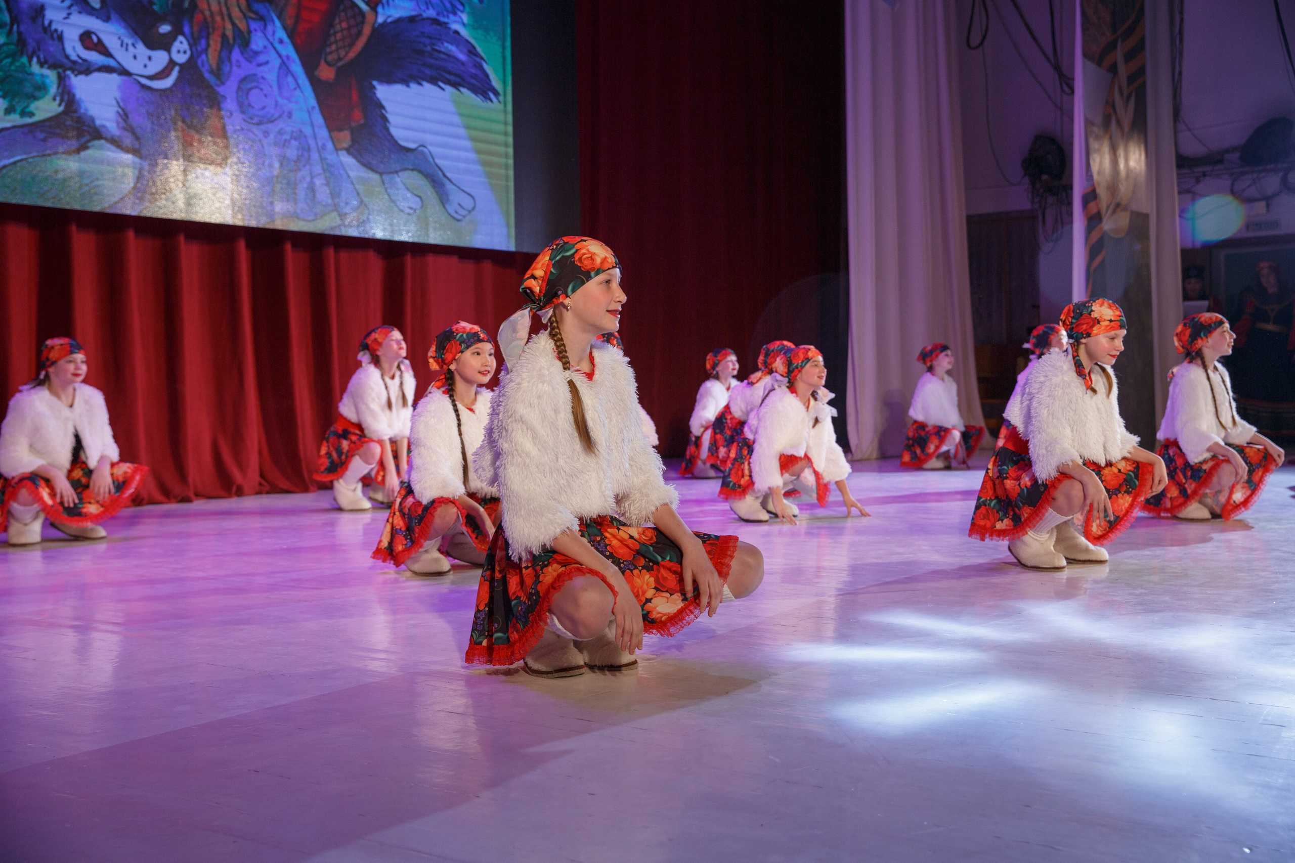 Девочки в сценических костюмах сидят на сцене во время представления.