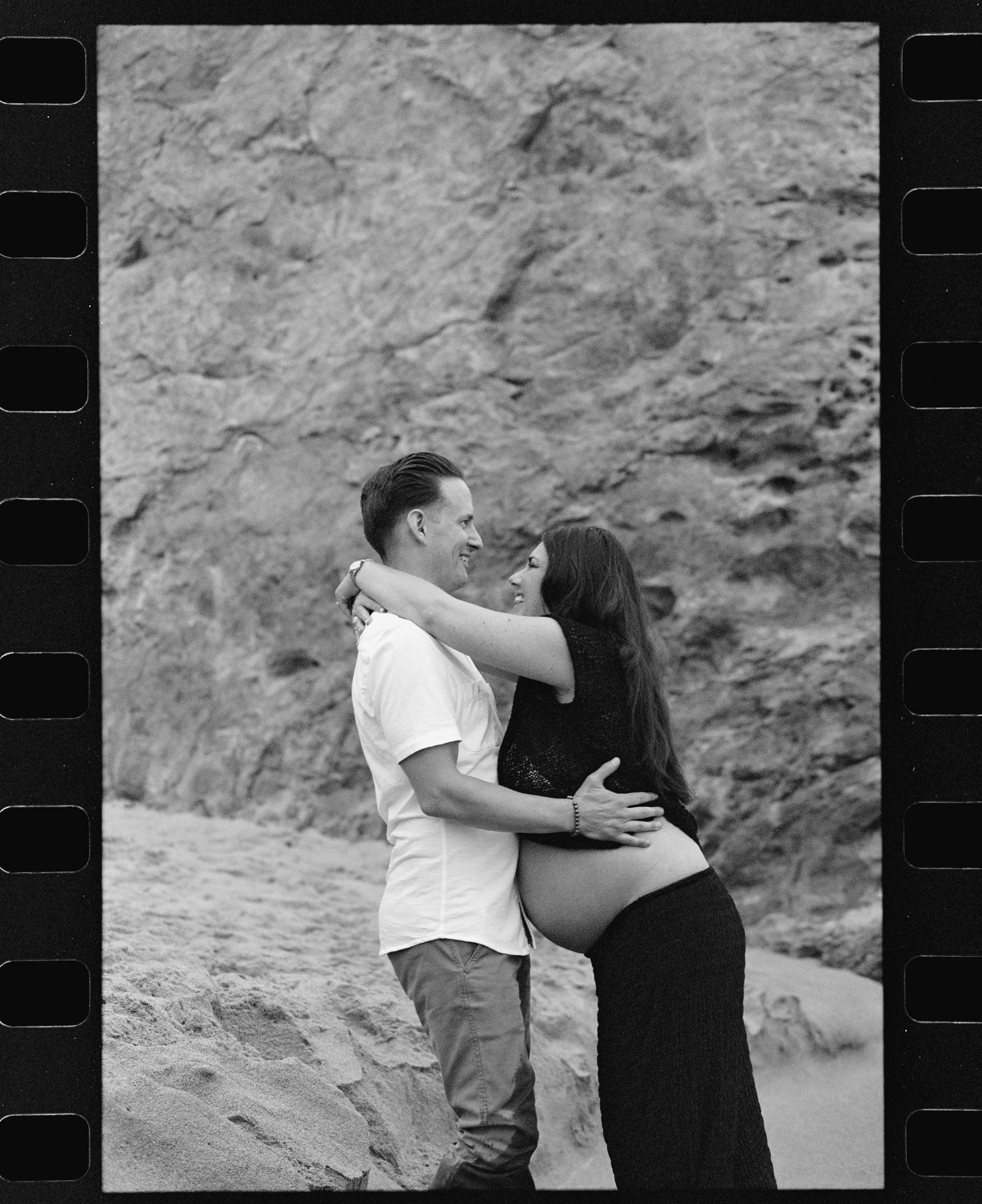 couples bumping bellies during maternity photoshoot on the beach