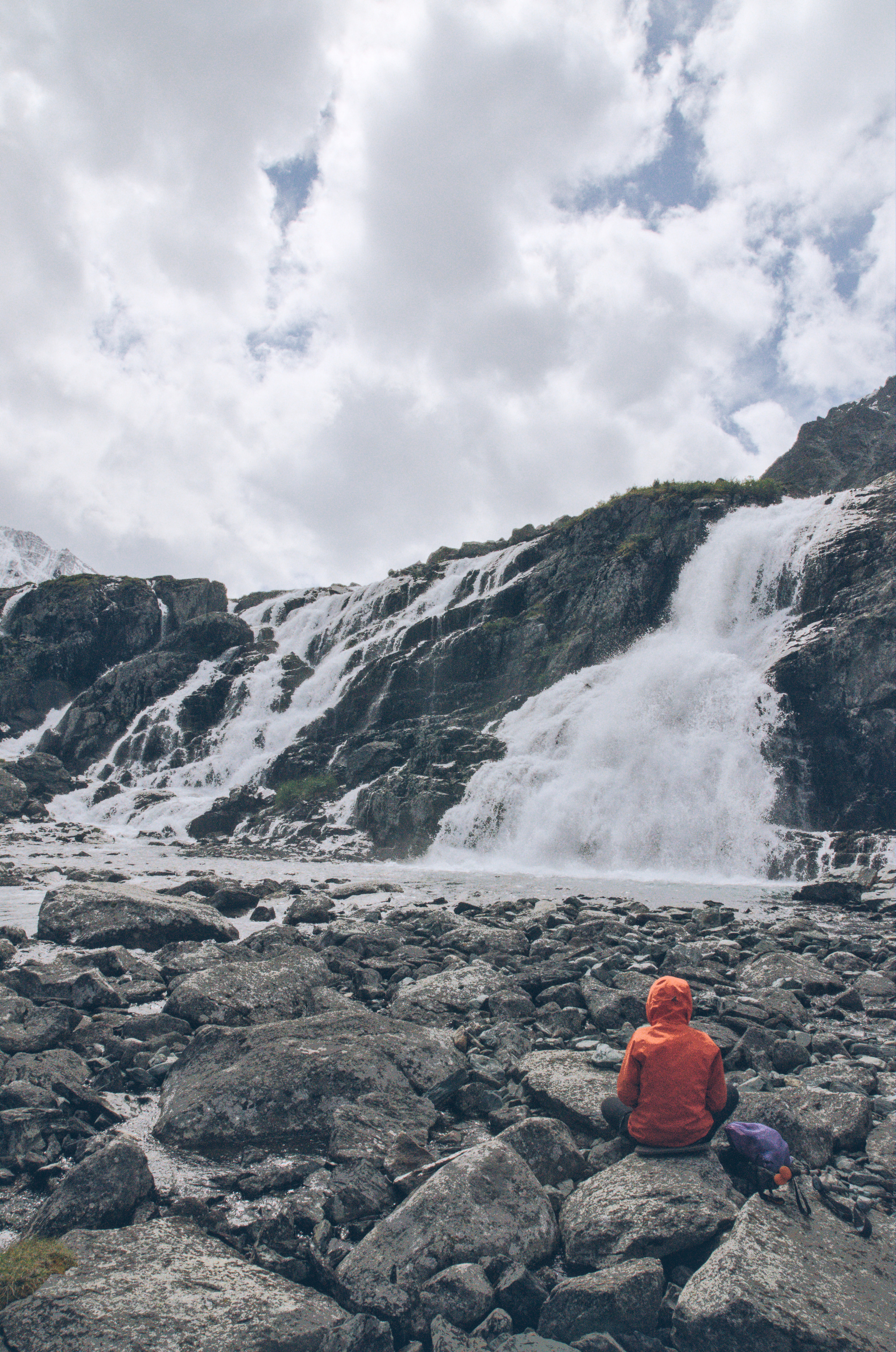 Человек сидящий на камнях на фоне водопада. Алтай