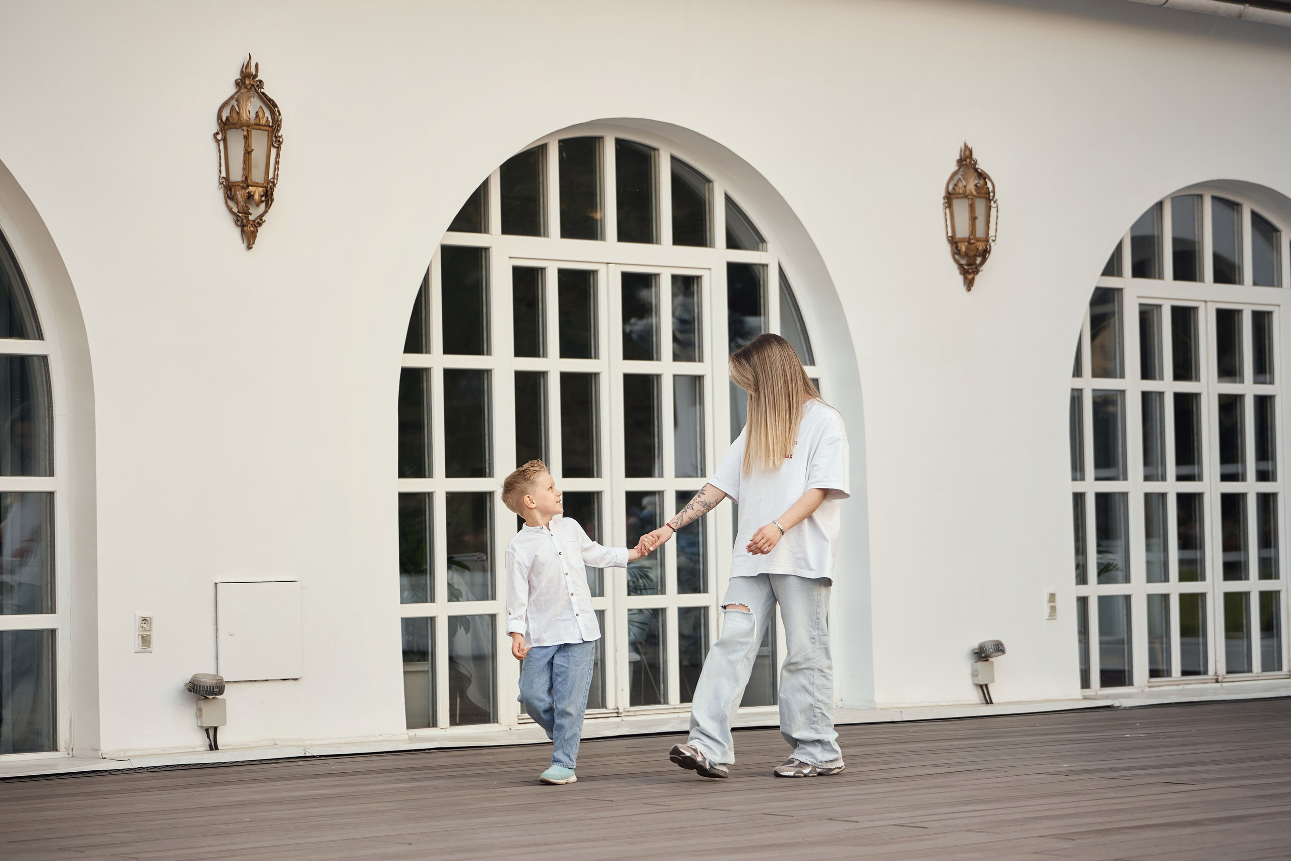 мама с сыном гуляют вдоль красивой стены с полукруглым окном