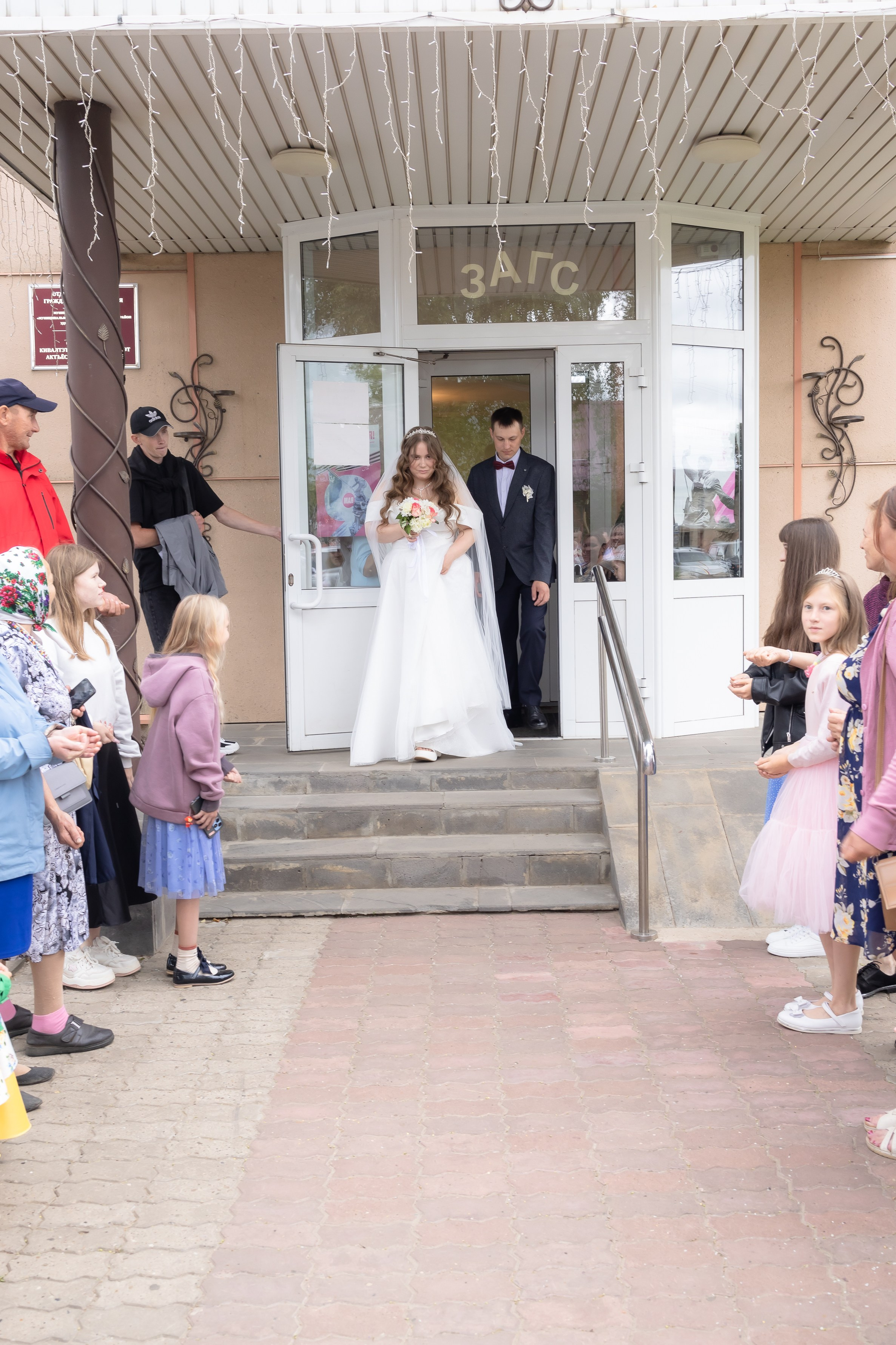 Молодожены выходят из ЗАГСа после регистрации, на улице их встречают родственники и друзья и кидают в них рис и конфетти разноцветные