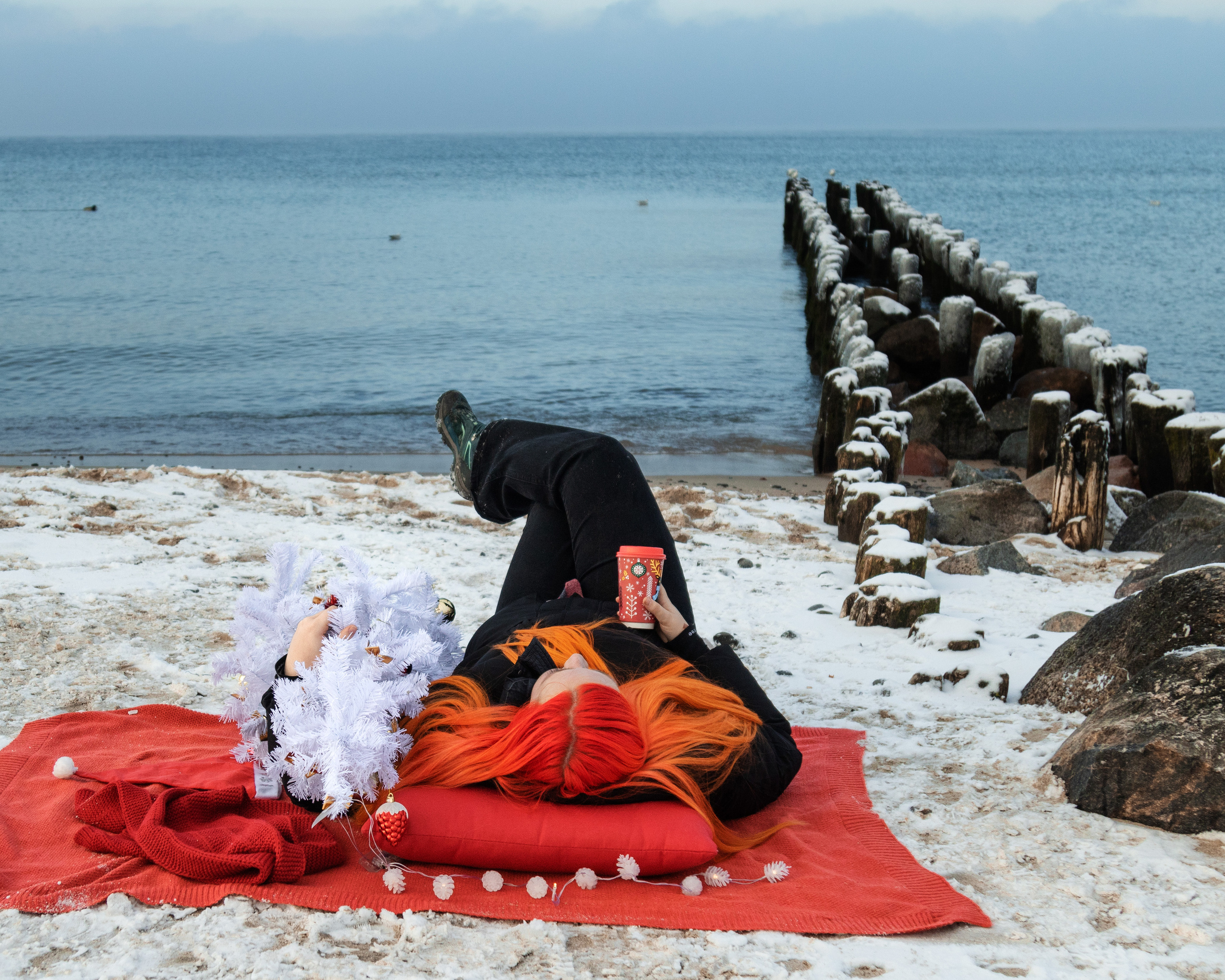 девушка лежит на красном пледе в обнимку с ёлкой на берегу моря