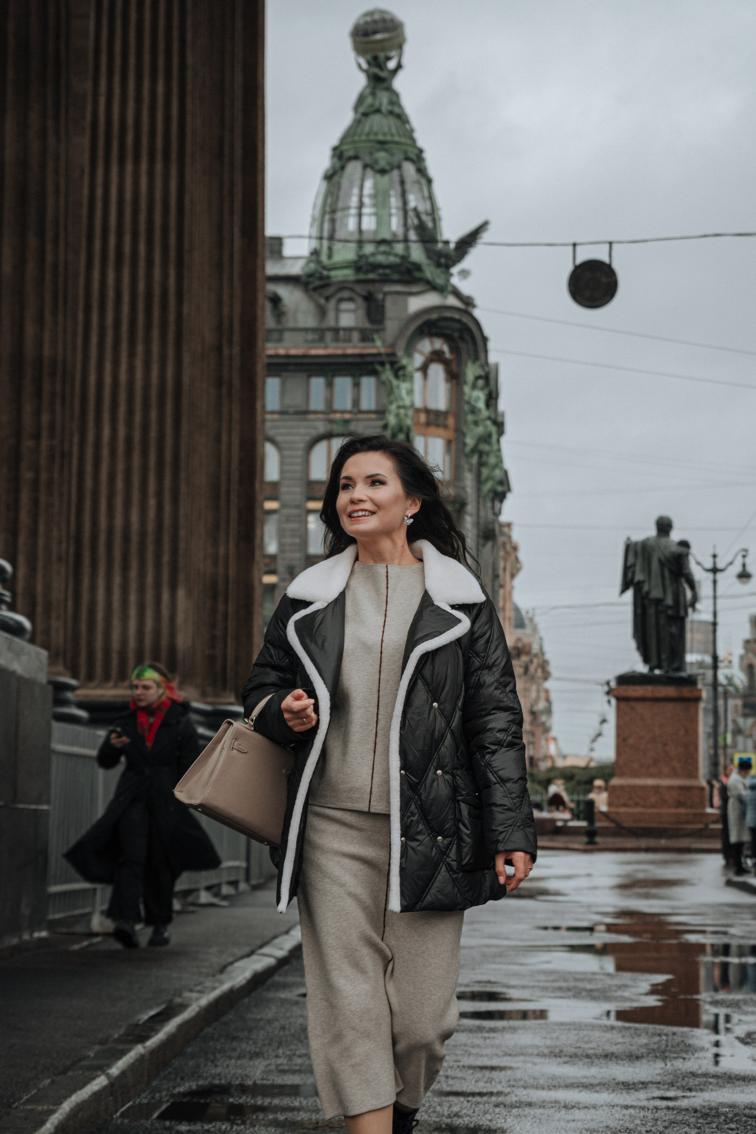 Девушка в стильном осеннем наряде прогуливается по Петербургу. В фоне виднеется известный Дом Зингера, который добавляет элегантности и авторитетности всему снимку.