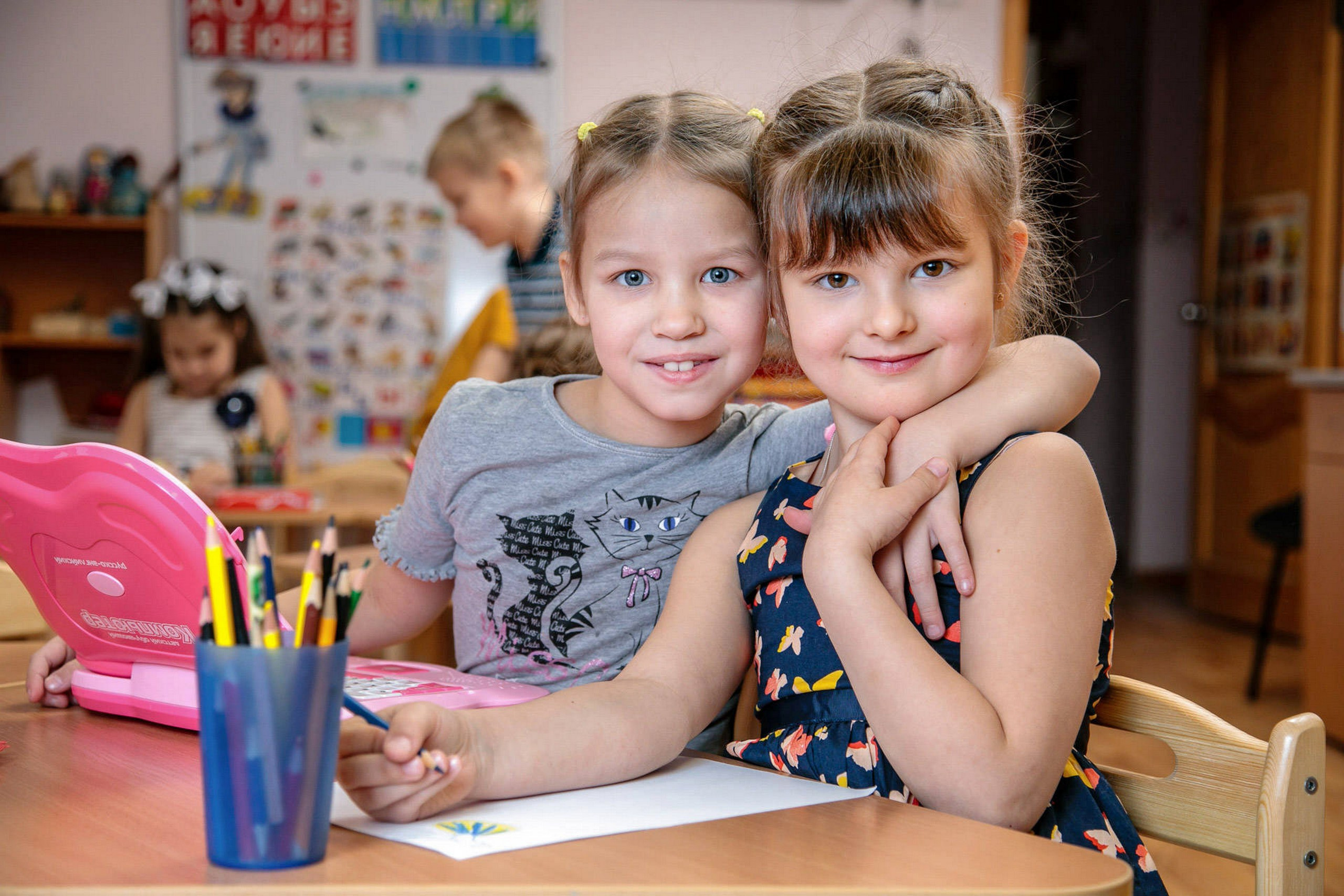 две подружки обнимаются за столом и фотографируются в группе