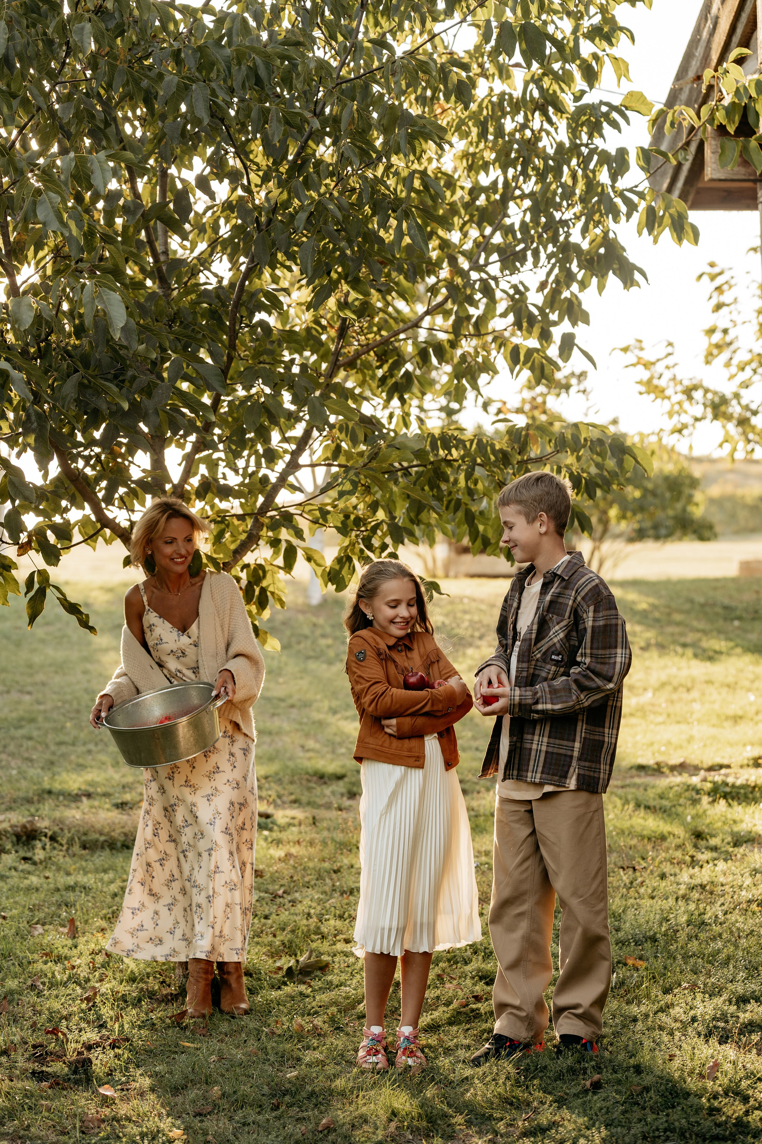 Семейные фотографии в Анапе на ферме: мама, сын и дочь собирают спелые яблоки в корзину. Фотограф Анапа.