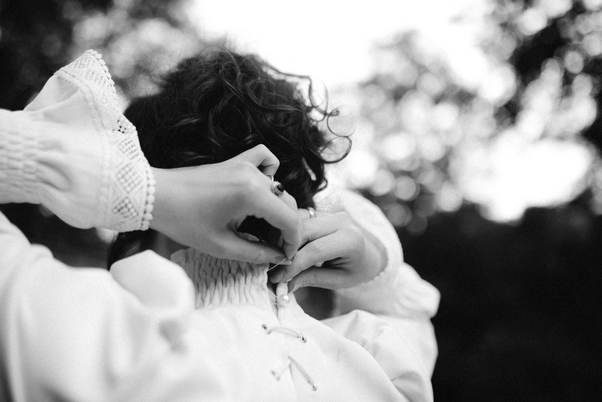 Девушка с черными волосами застегивает воротничок своего белого платья