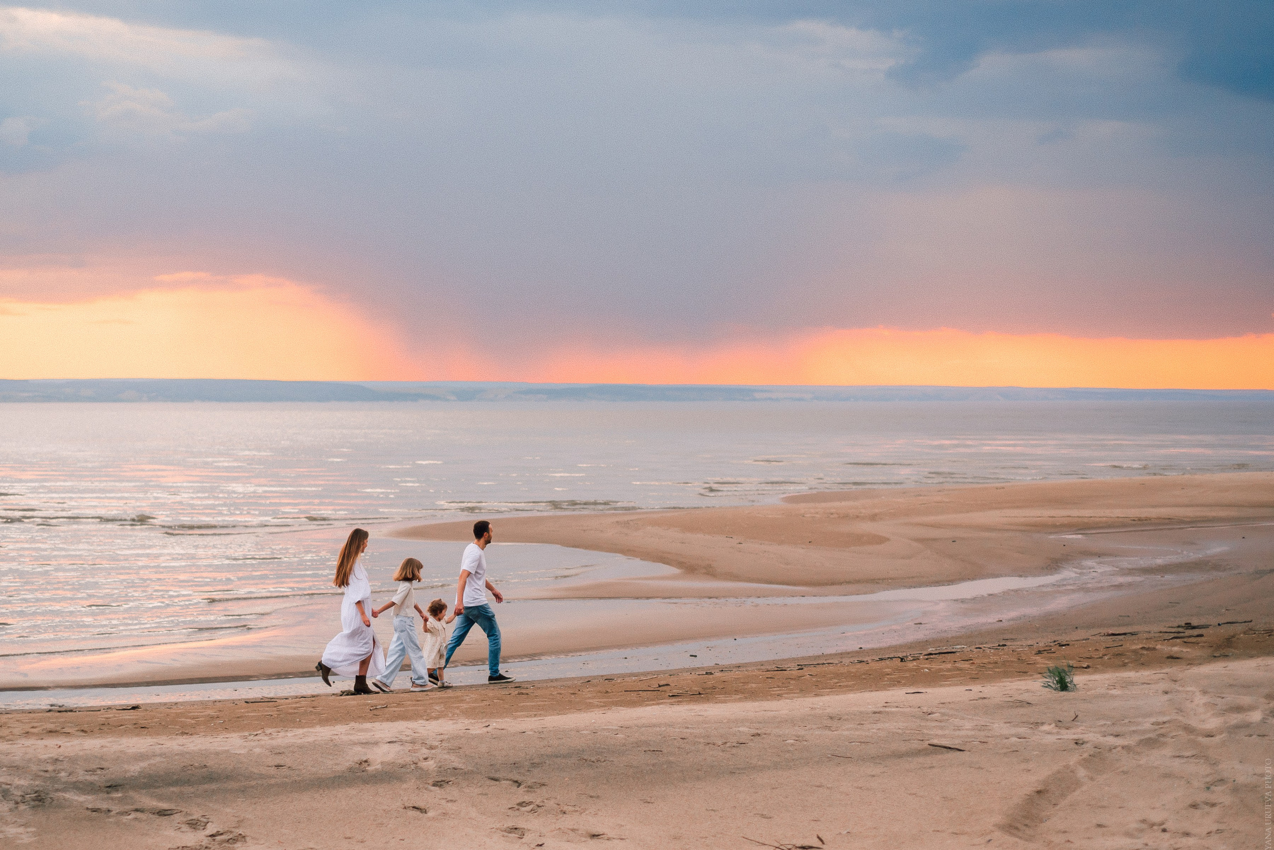 Семья бежит по пляжу на закате