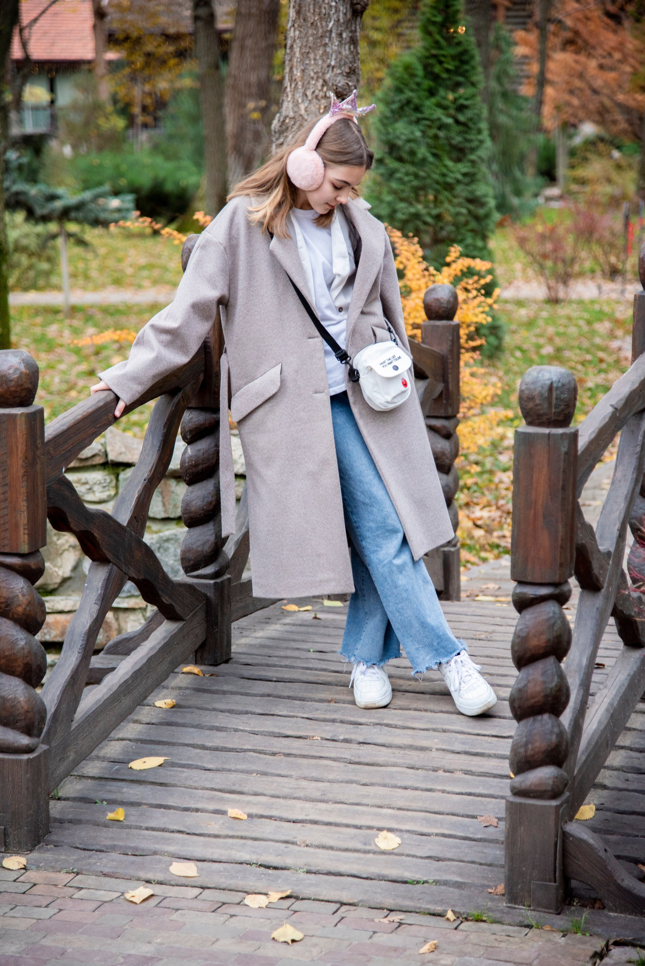 Девушка на мостике, наушники, пальто, джинсы, белые кроссовки. парк лога. осень