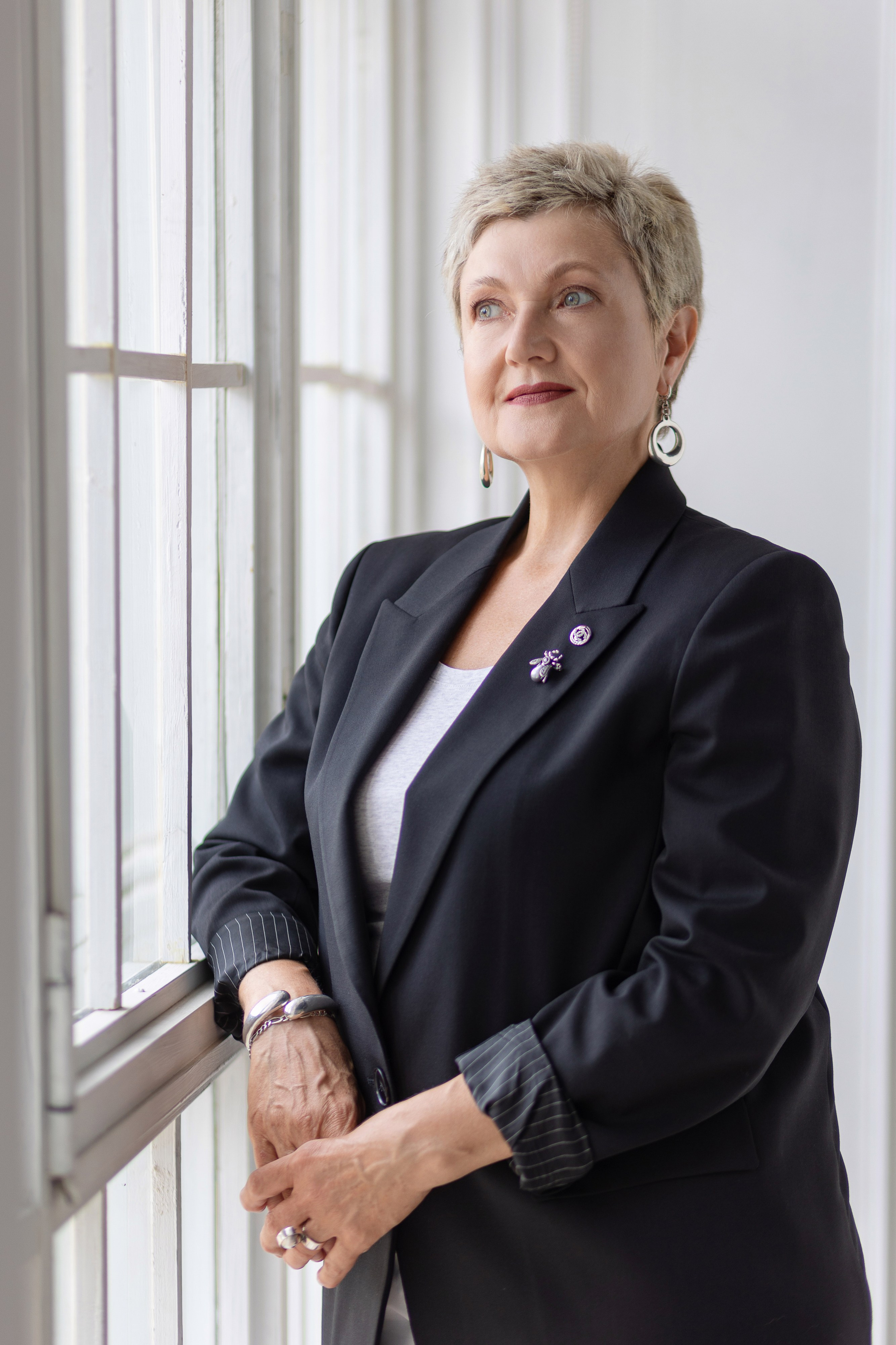 Женщина  стоит у окна и смотрит в него.