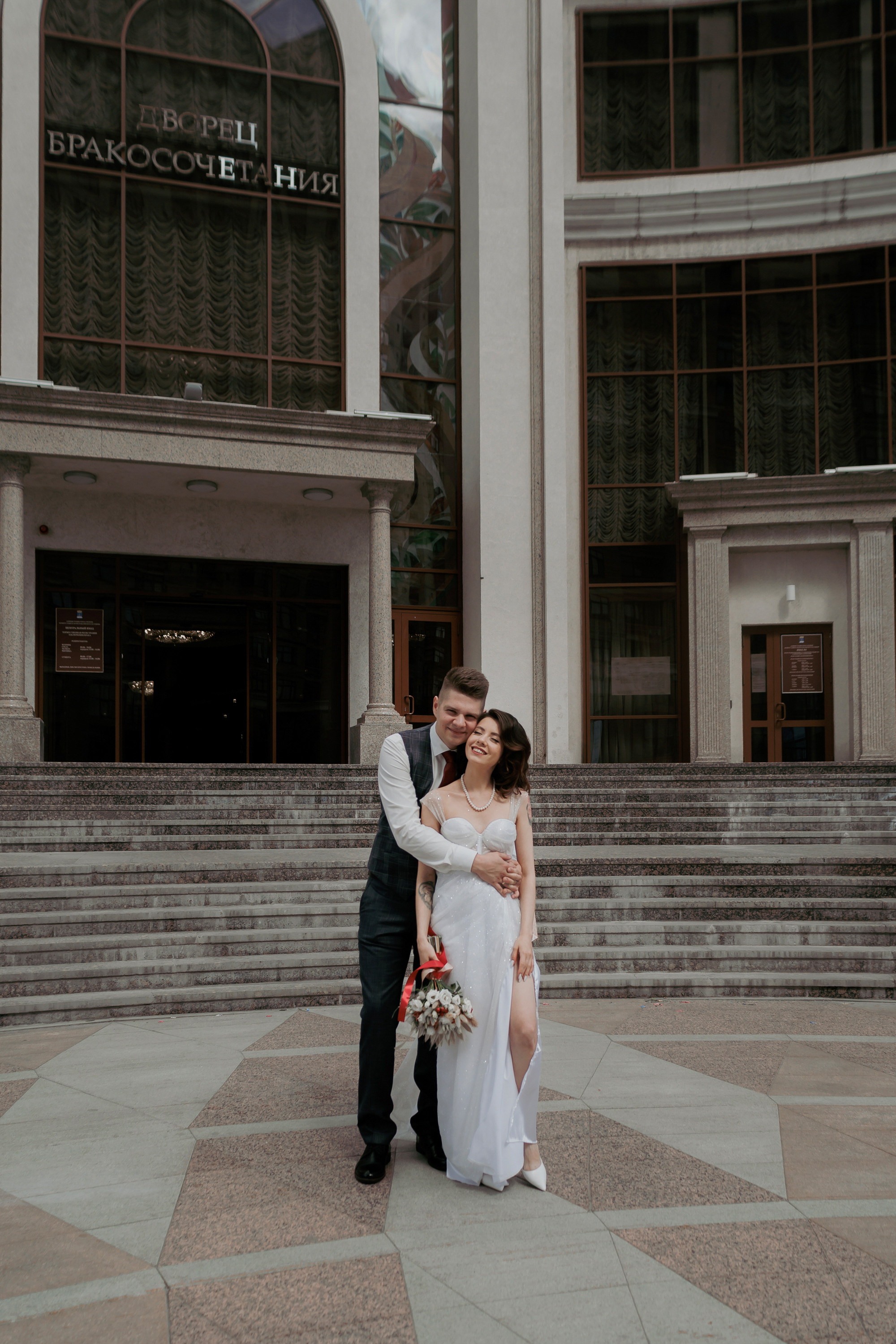 Жених и невеста обнимаются у дворца бракосочетания