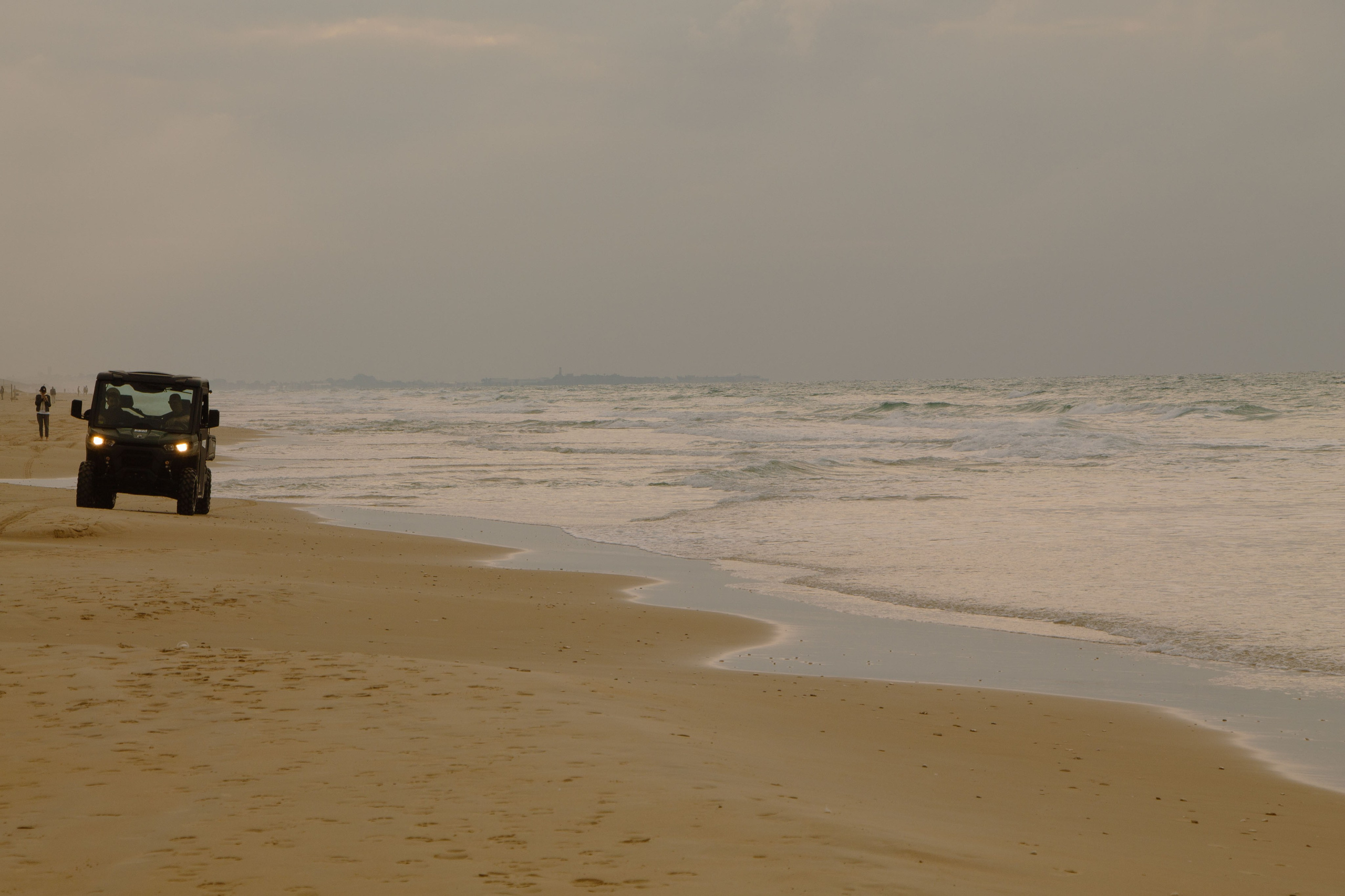 берег моря, едет маленькая машина с включёнными фарами