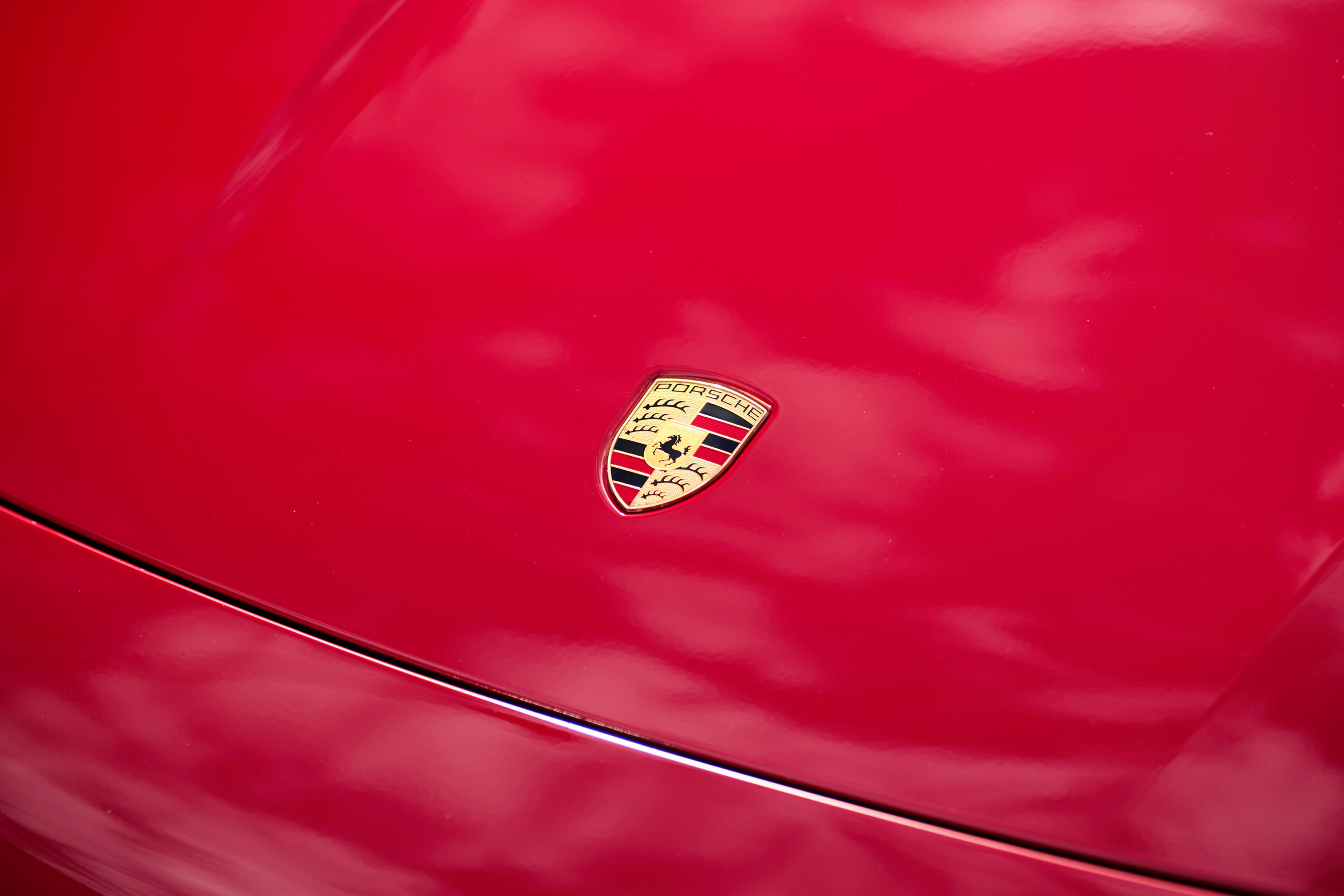 Эмблема Porsche на капоте красного Porsche Taycan GTS крупным планом