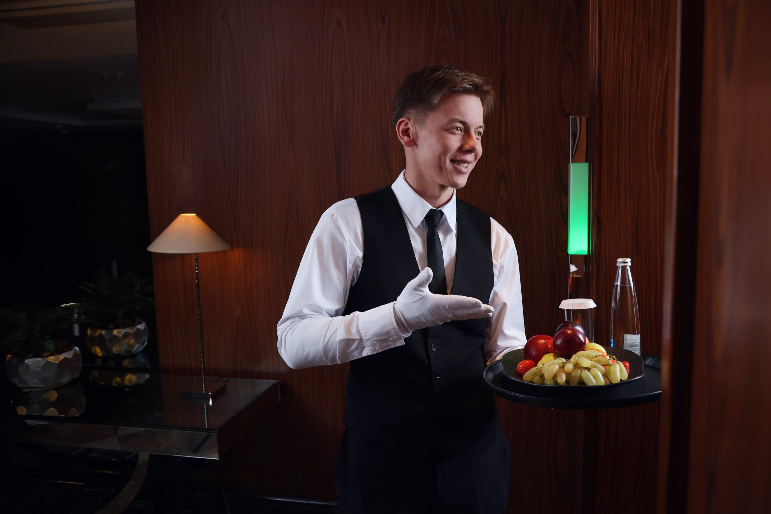 Официант службы room-service доставил ужин в номер и улыбается, создавая гостеприимное впечатление.