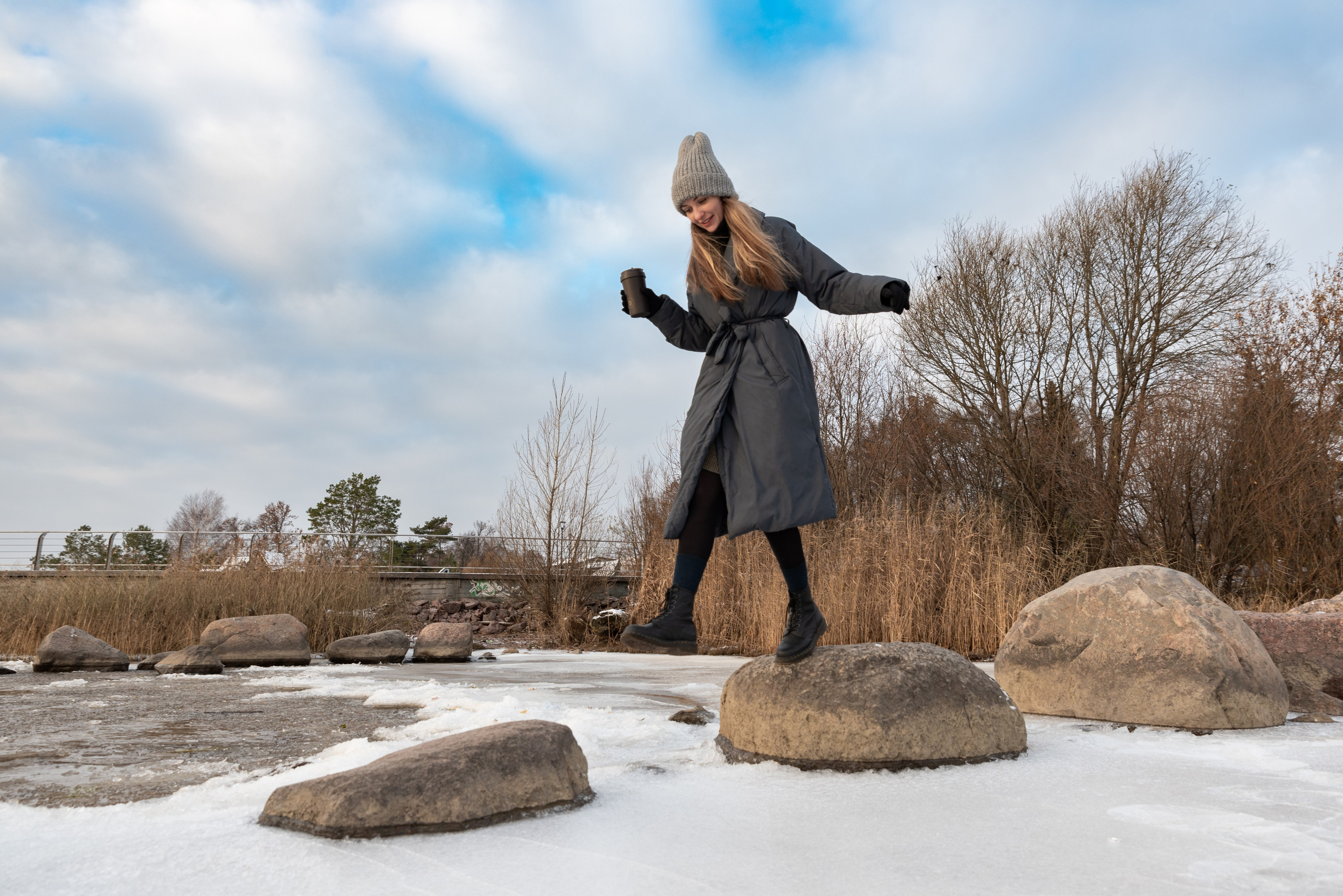 Зима, Финский залив, побережье. Камни торчат изо льда. Девушка перепрыгивает с камня на камень.