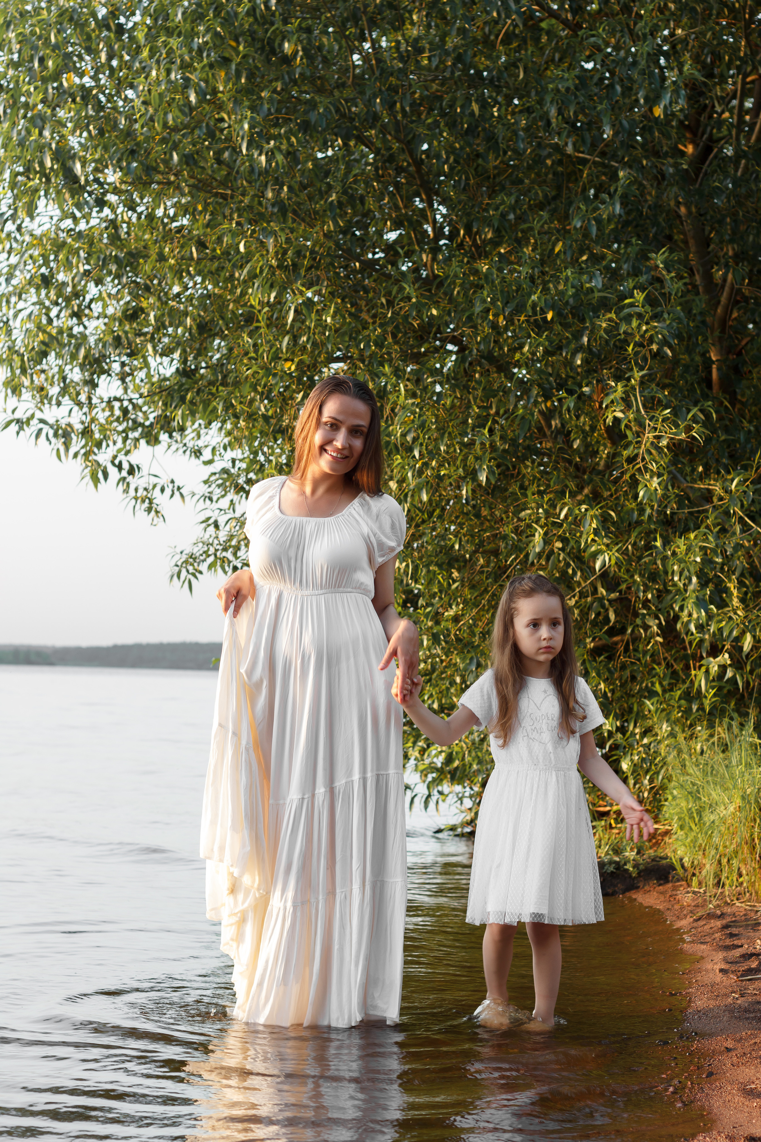 Мама и дочка гуляют босиком по воде на заливе