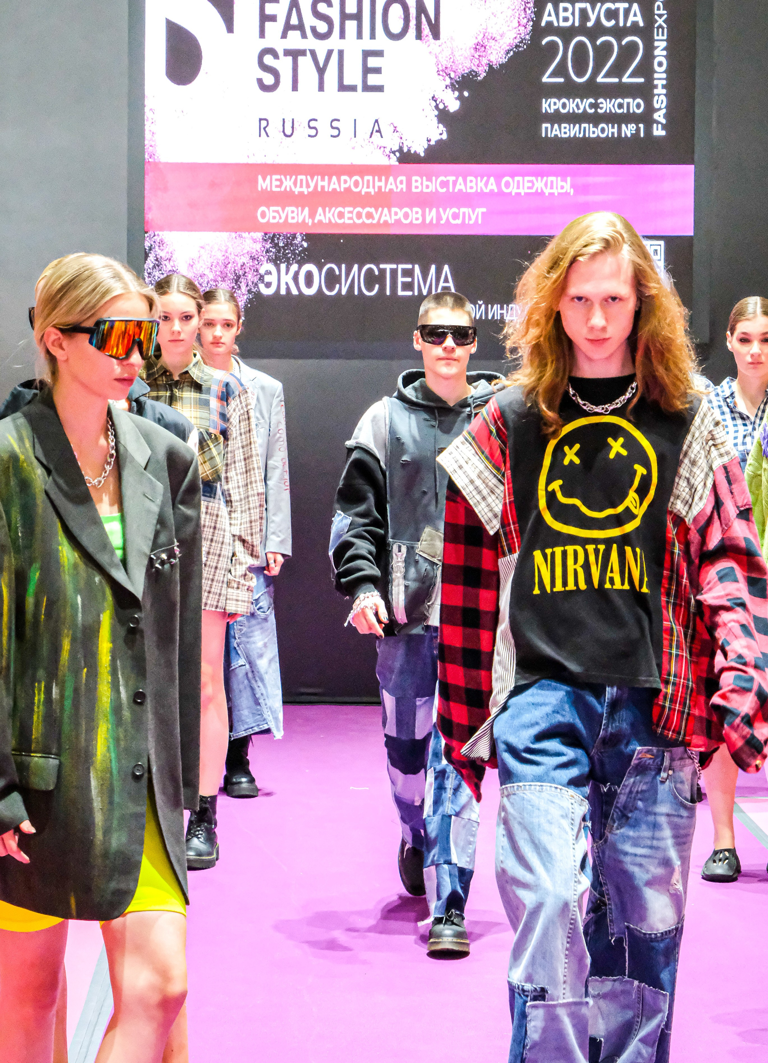  "Модели в ярких нарядах проходят по подиуму во время показа мод, освещенные яркими софитами и окруженные восторженными зрителями."