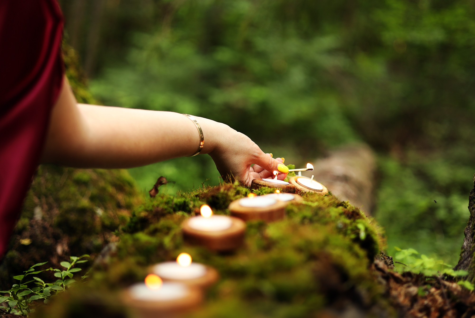 девушка зажигает свечи правой рукой в лесу на тематической фотосессии 