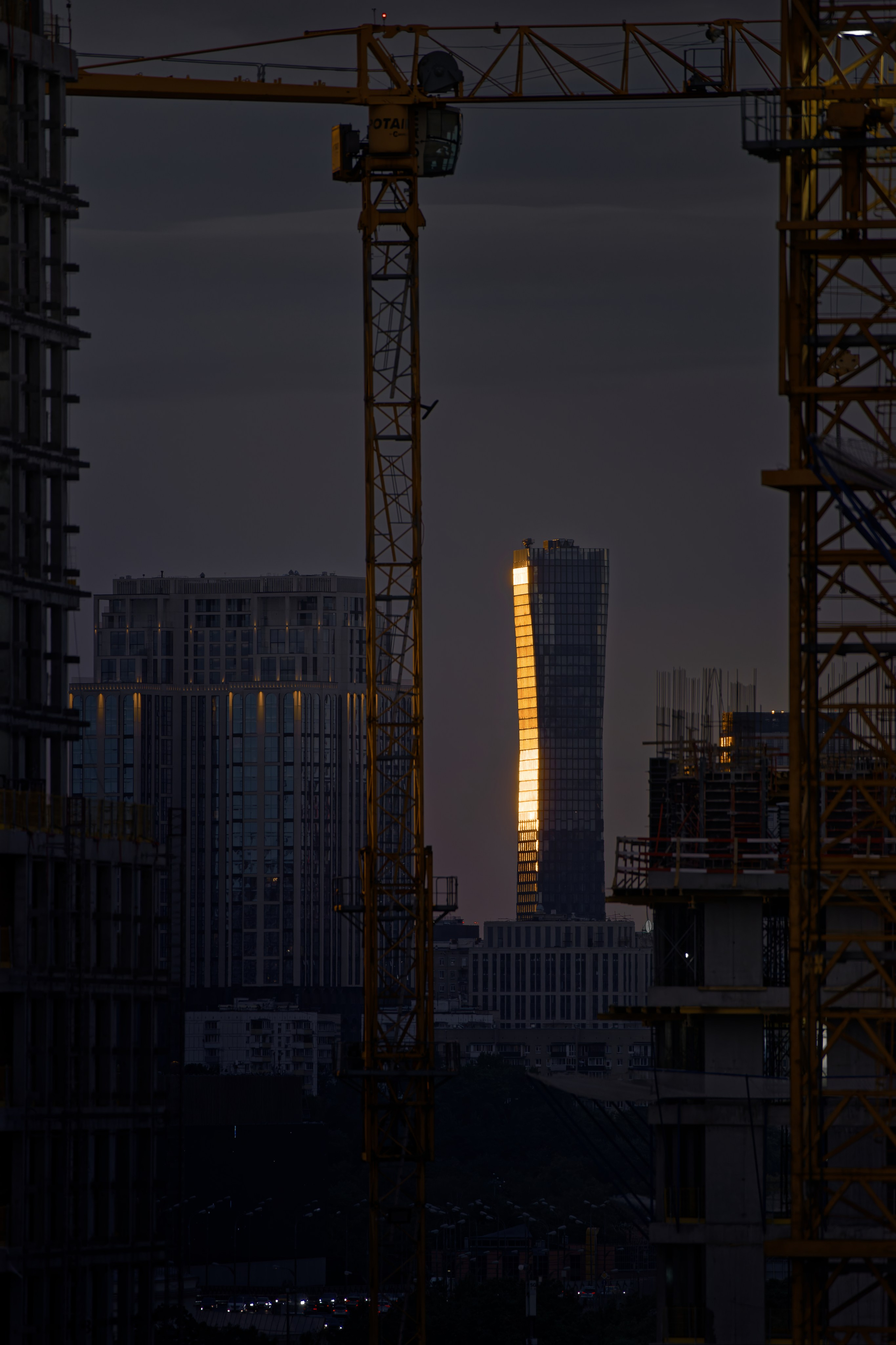 Вид через строительные леса на сияющий в закатных лучах небоскреб на фоне серого неба