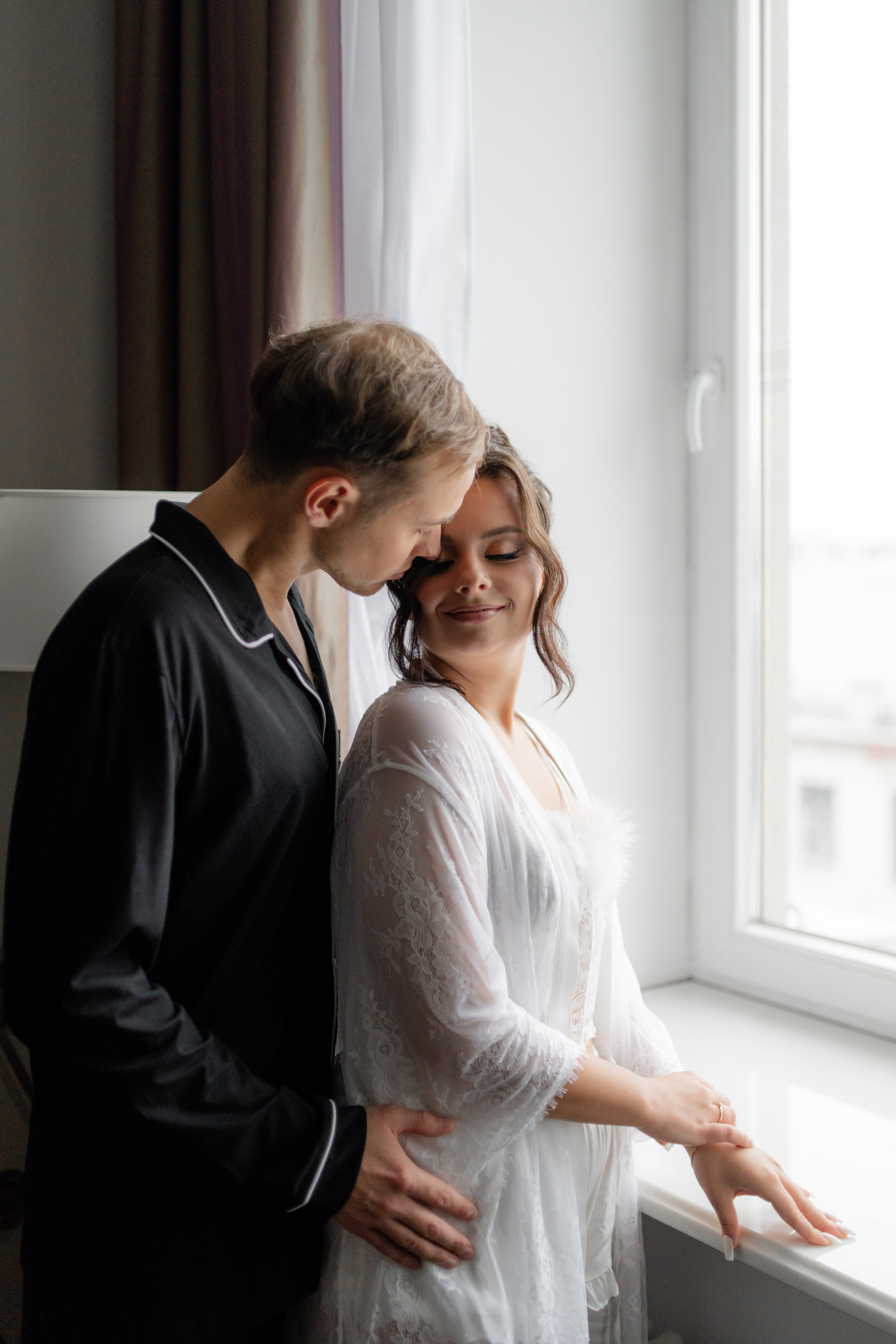 Утро невесты. Жених обнимает невесту у окна в отеле
