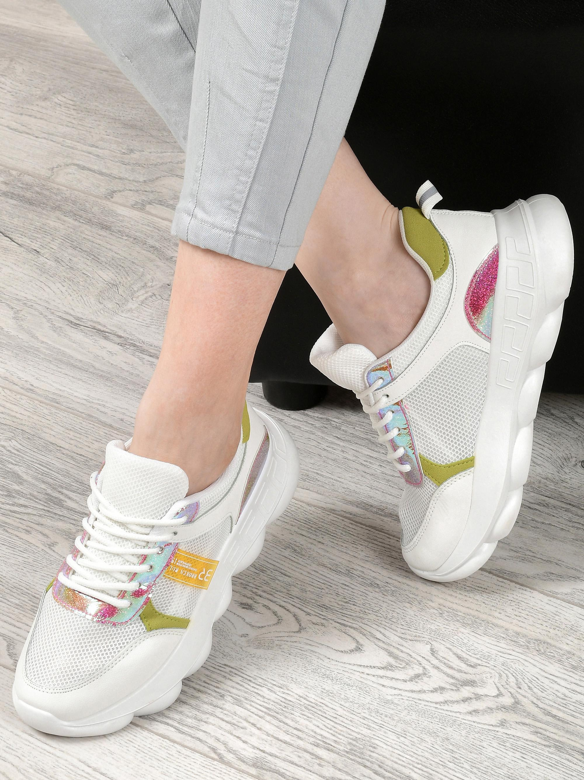 Модель в белых кроссовках с цветными вставками на деревянном полу в фотостудии.