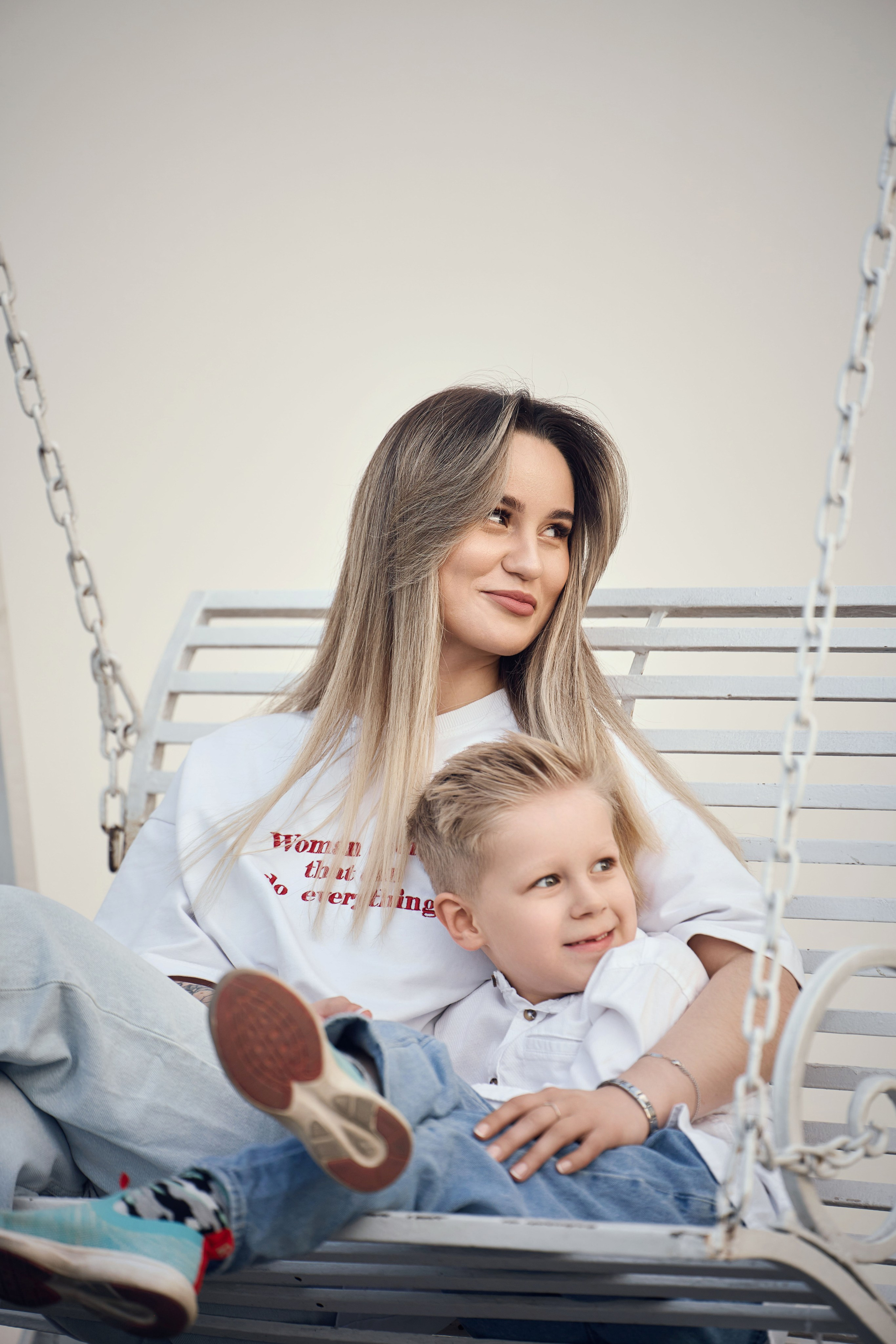 мама с маленьким сыном качаются на лавочке качелях