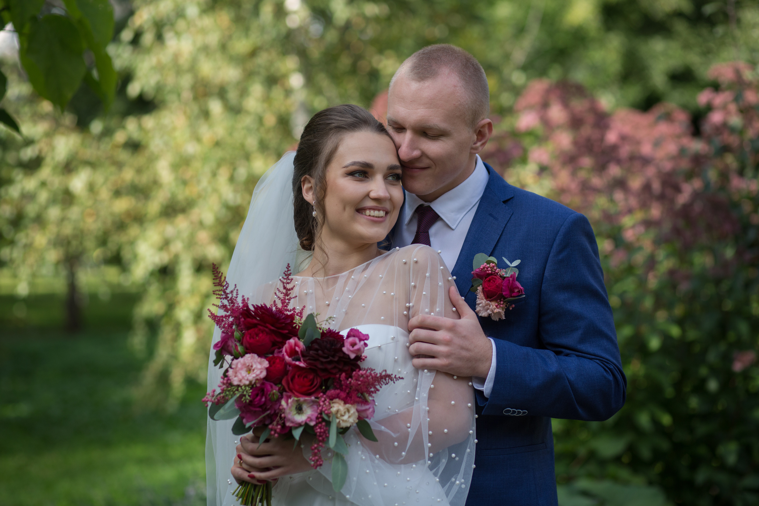 жених обнимает невесту за плечи и смотрит на ее улыбку. на заднем фоне зеленые березы