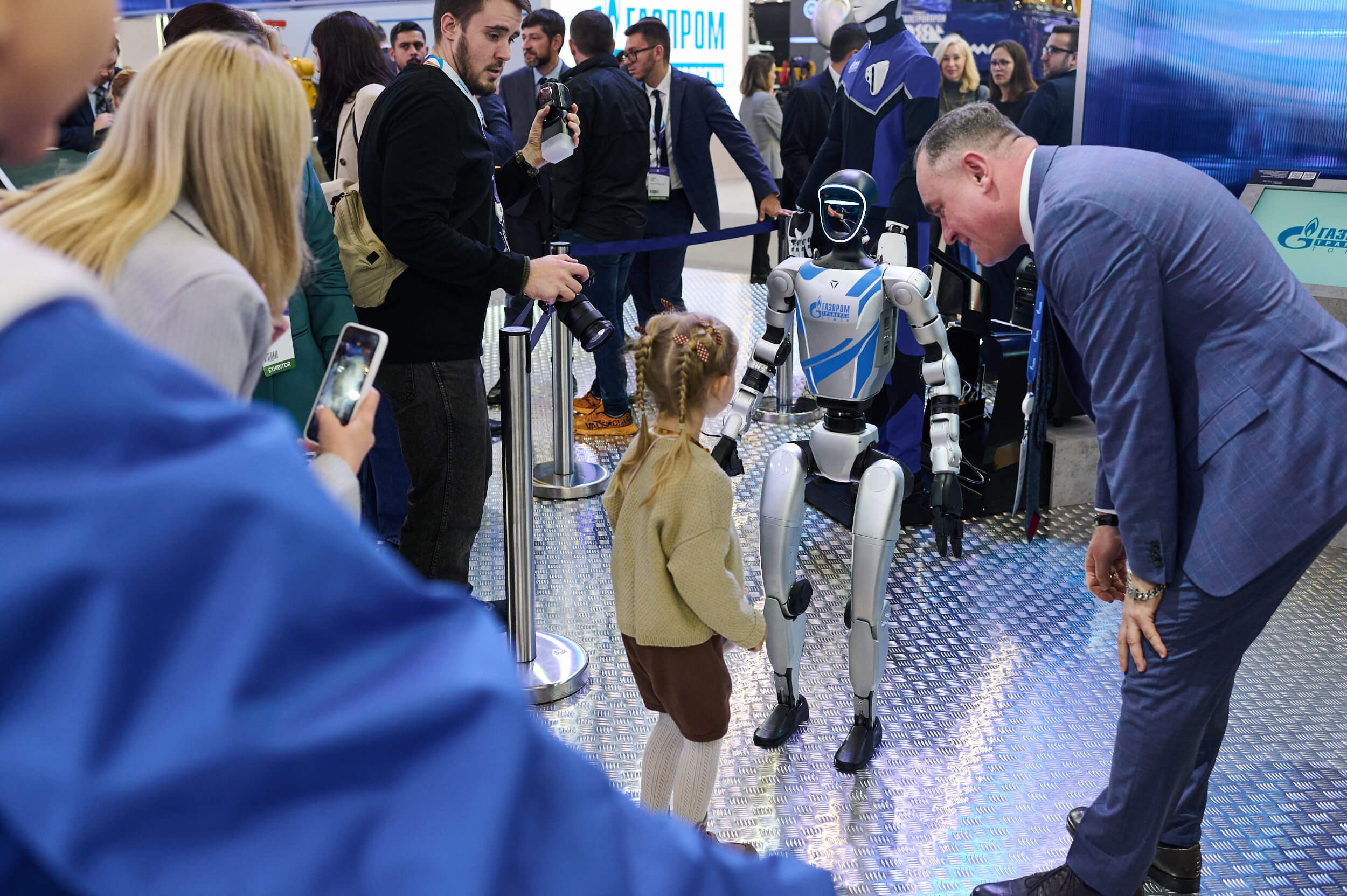 Маленькая девочка рассматривает робота на выставочном стенде Петербургского международного газового форума 2025 в Экспофоруме
