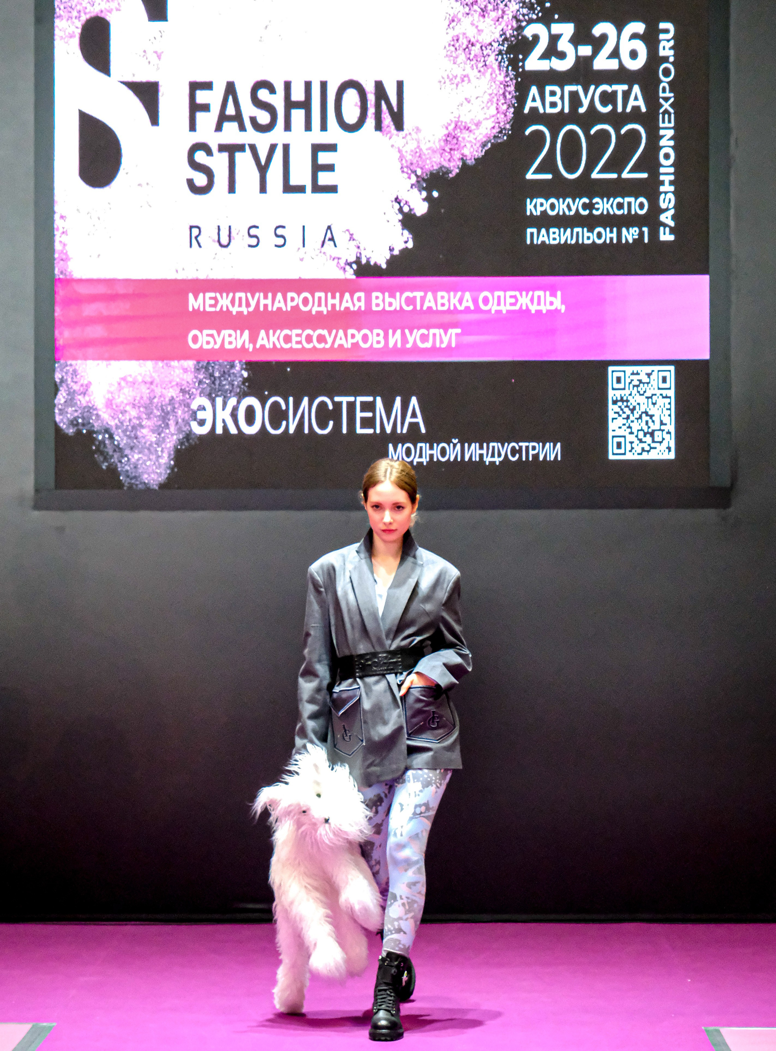  "Модели в ярких нарядах проходят по подиуму во время показа мод, освещенные яркими софитами и окруженные восторженными зрителями."