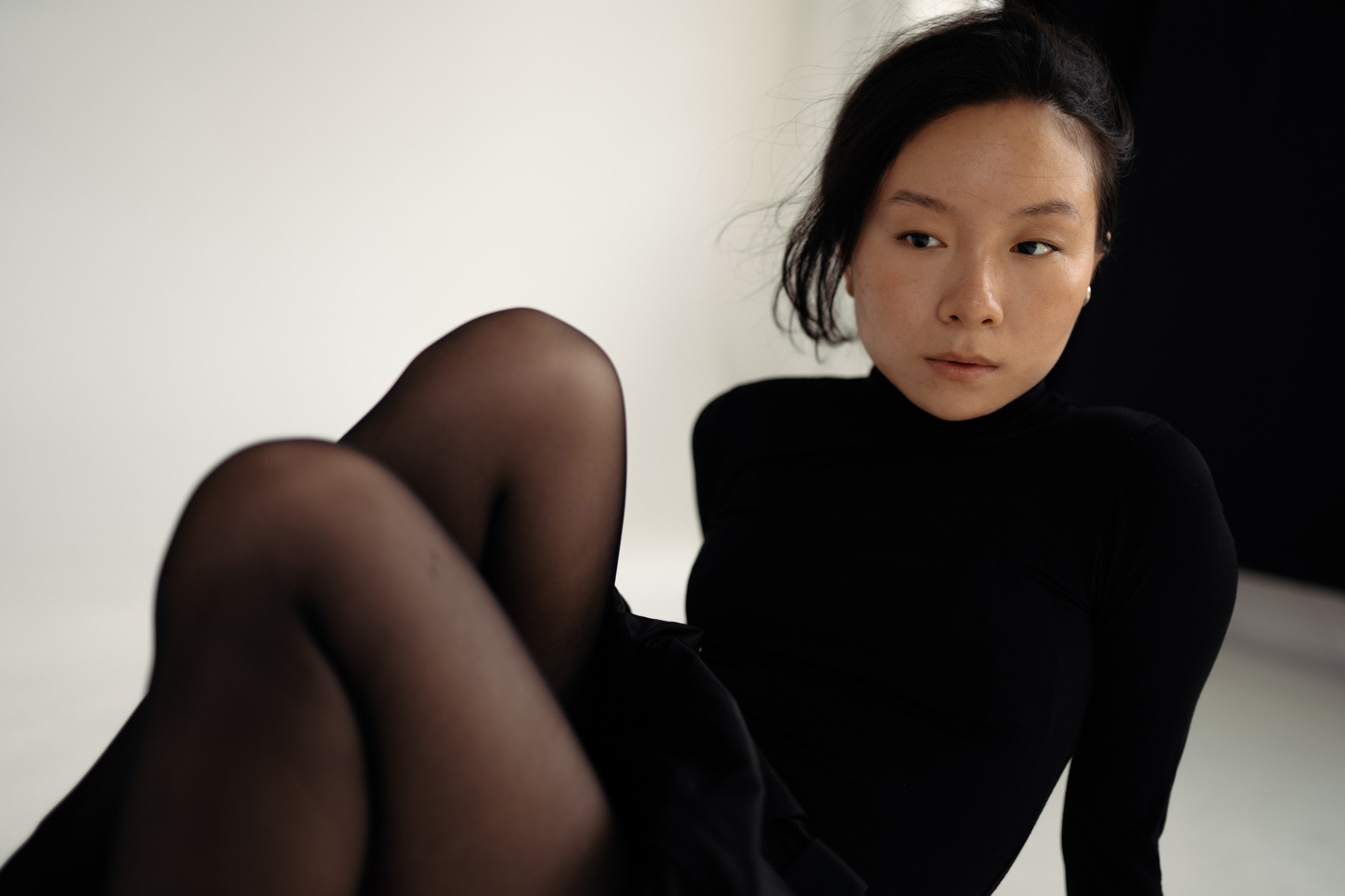 Модель в чёрном платье сидит в минимастичной студии на фоне светлой и чёрной стены, портретная фотосессия в Санкт-Петербурге