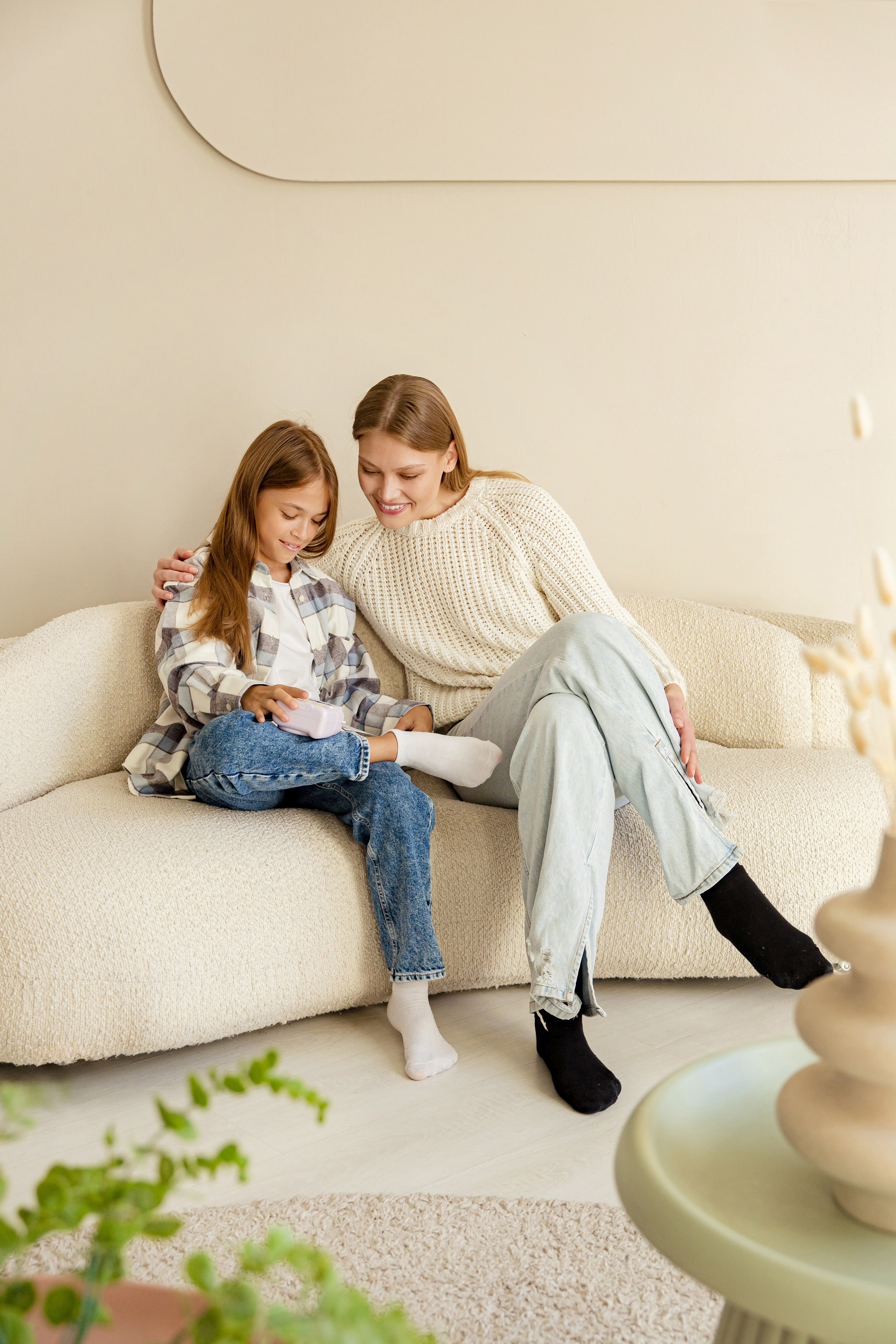 Сестры сидят на диване и рекламируют камеру моментальной печати