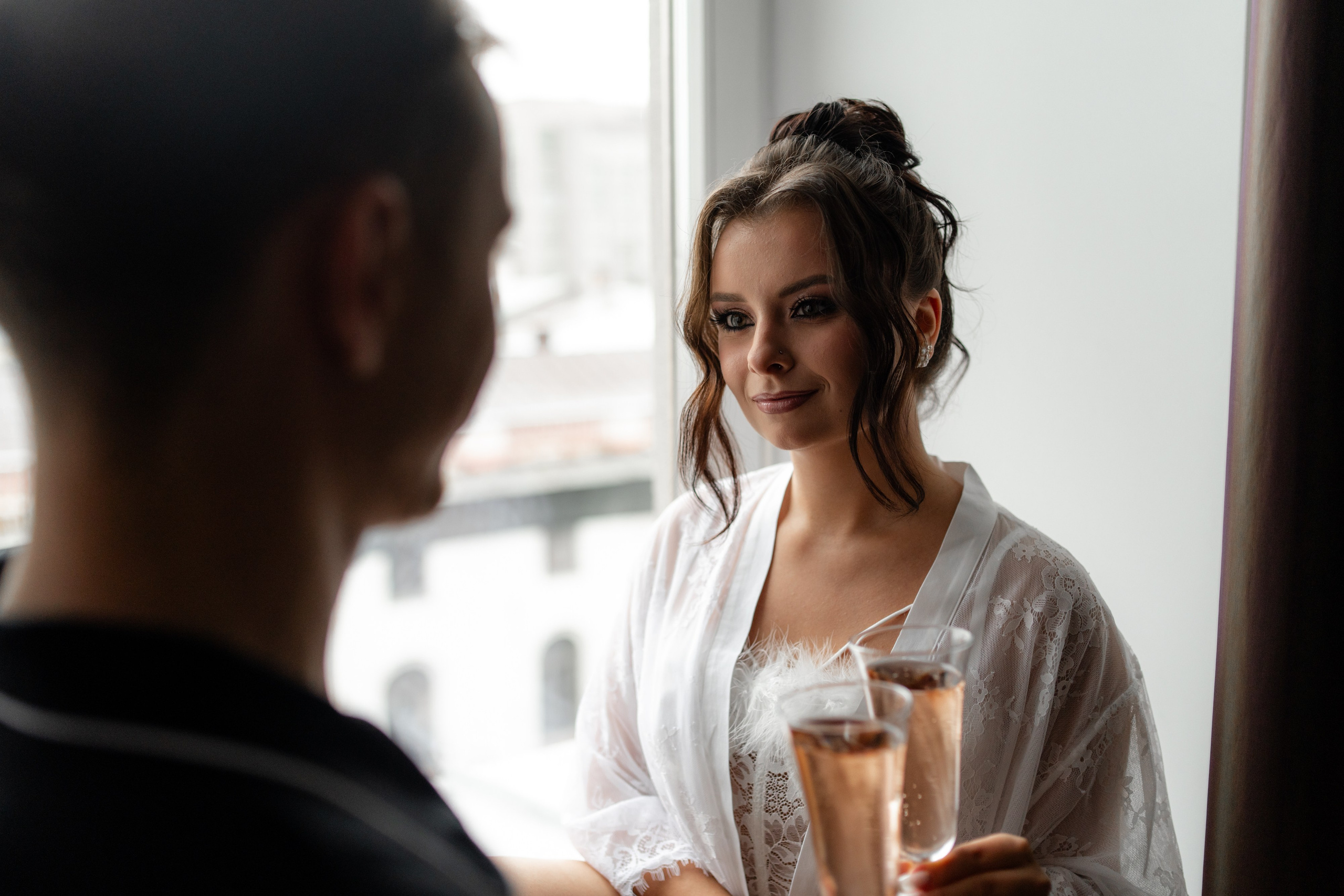 Утро невесты. Невеста смотрит на жениха с бокалом шампанского в отеле