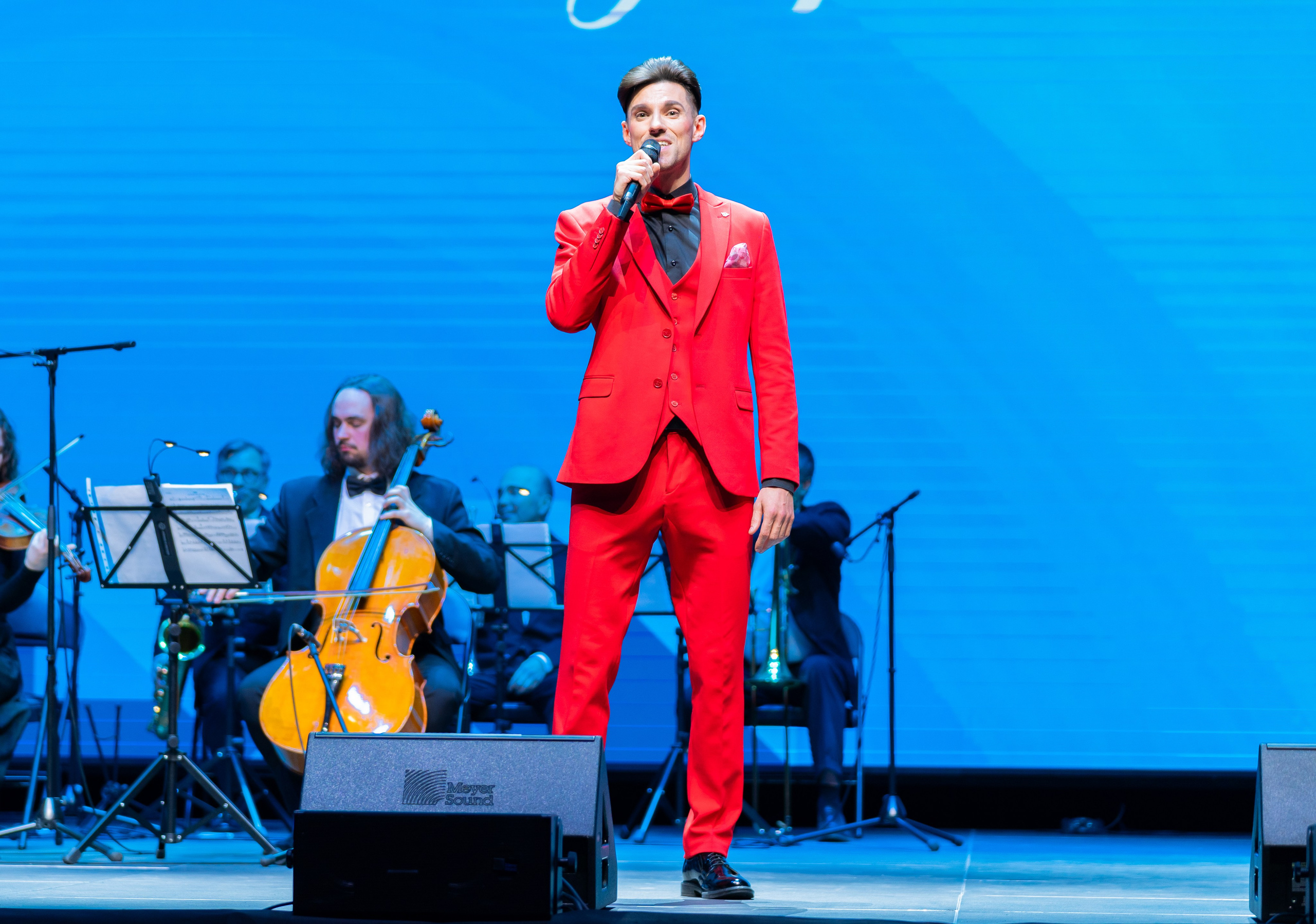 Солист в ярком красном костюме выступает с микрофоном на концерте в честь Дня местного самоуправления в Санкт-Петербурге | Фото: Евгений Мальцев.