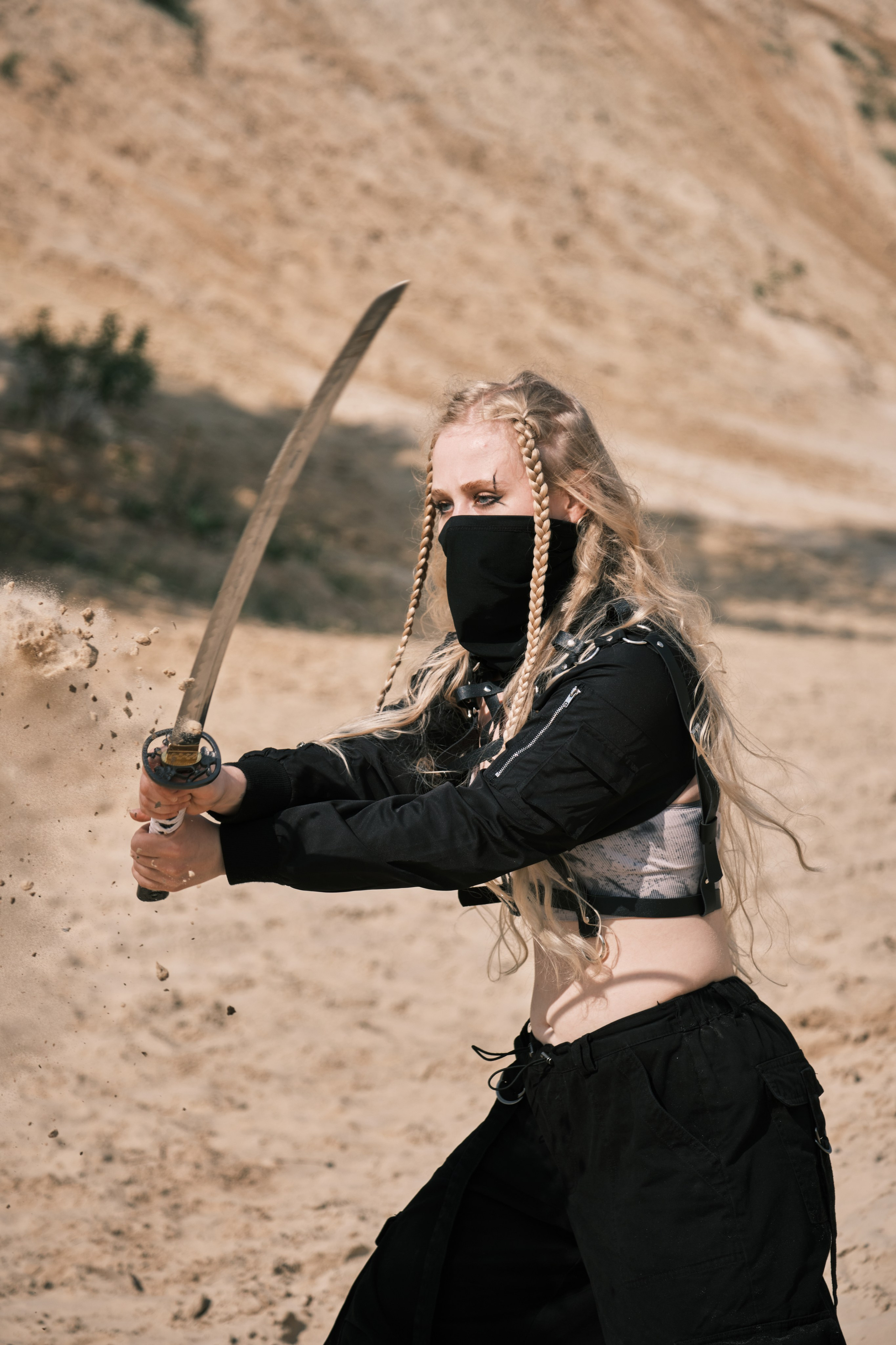 Светловолосая девушка с катаной в руке и черной маске на лице стоит в боевой стойке