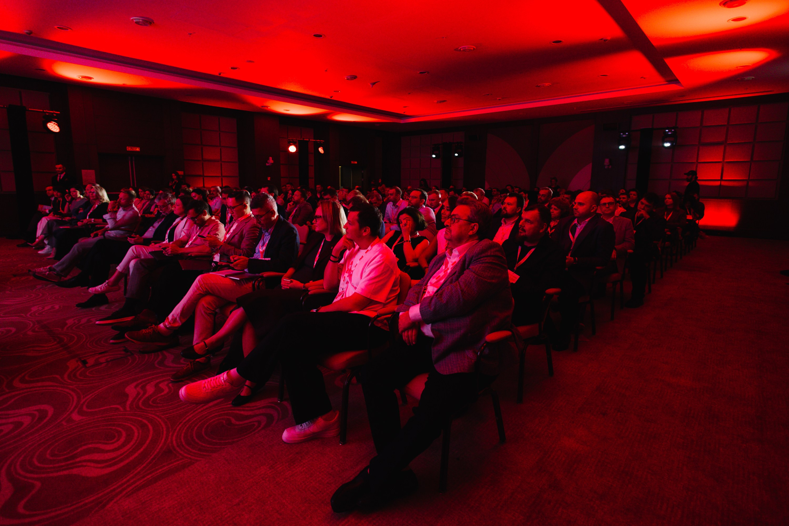 Масштаб: Вид со сцены на заполненный зрительный зал во время бизнес-конференции.