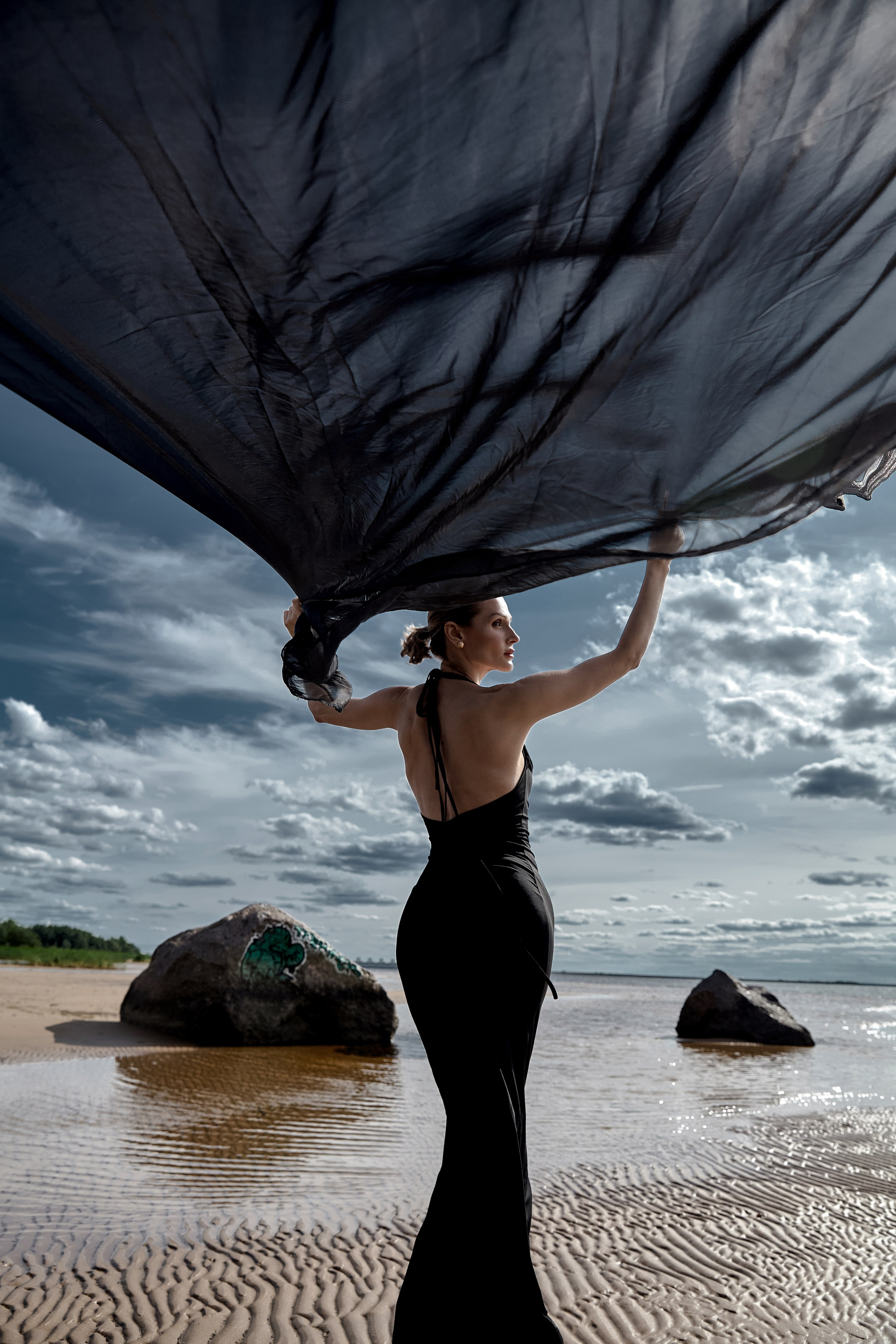силуэт женщины в черном с развивающейся тканью на финском заливе