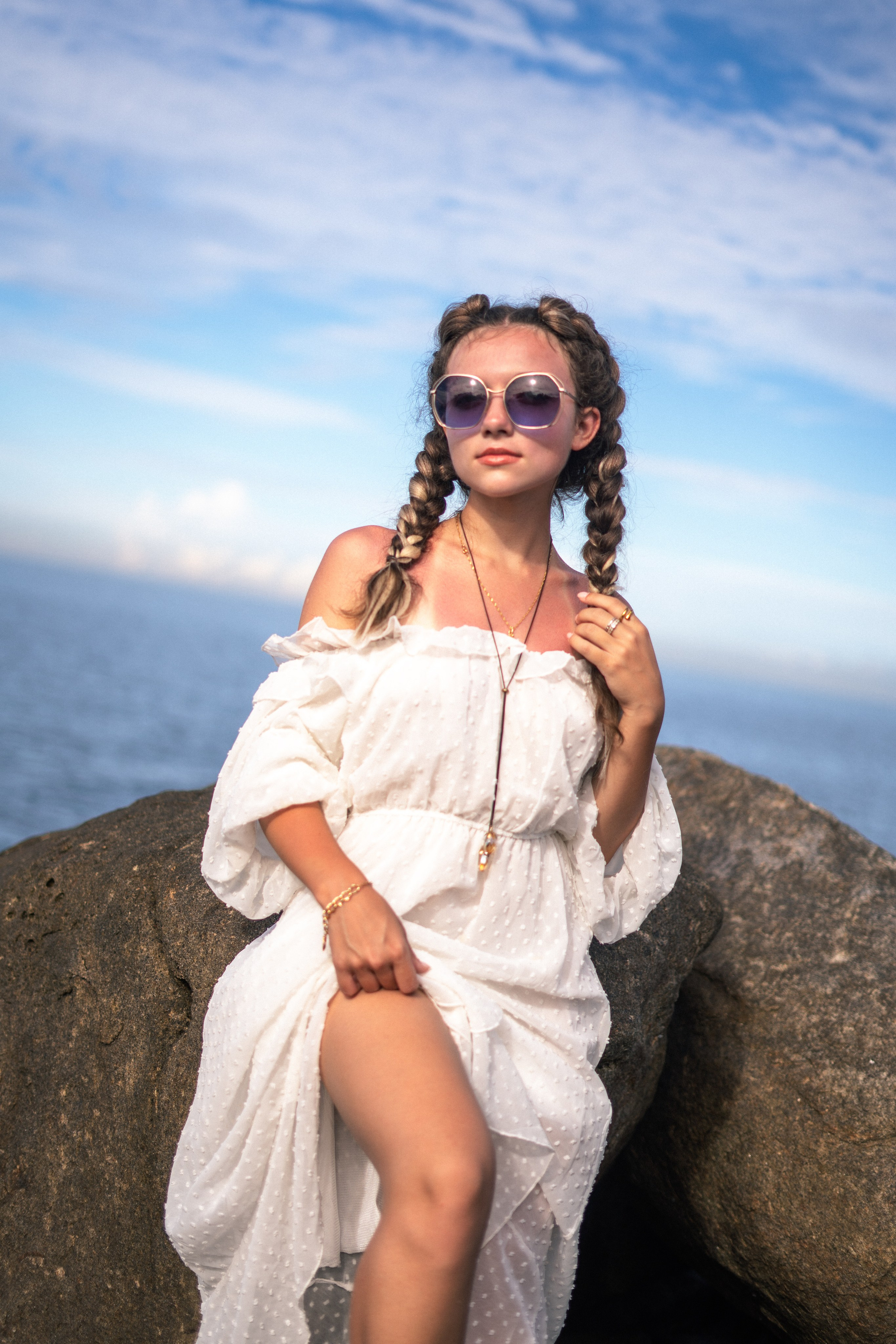 a young girl in a white dress and glasses with flowing hair on the rocks