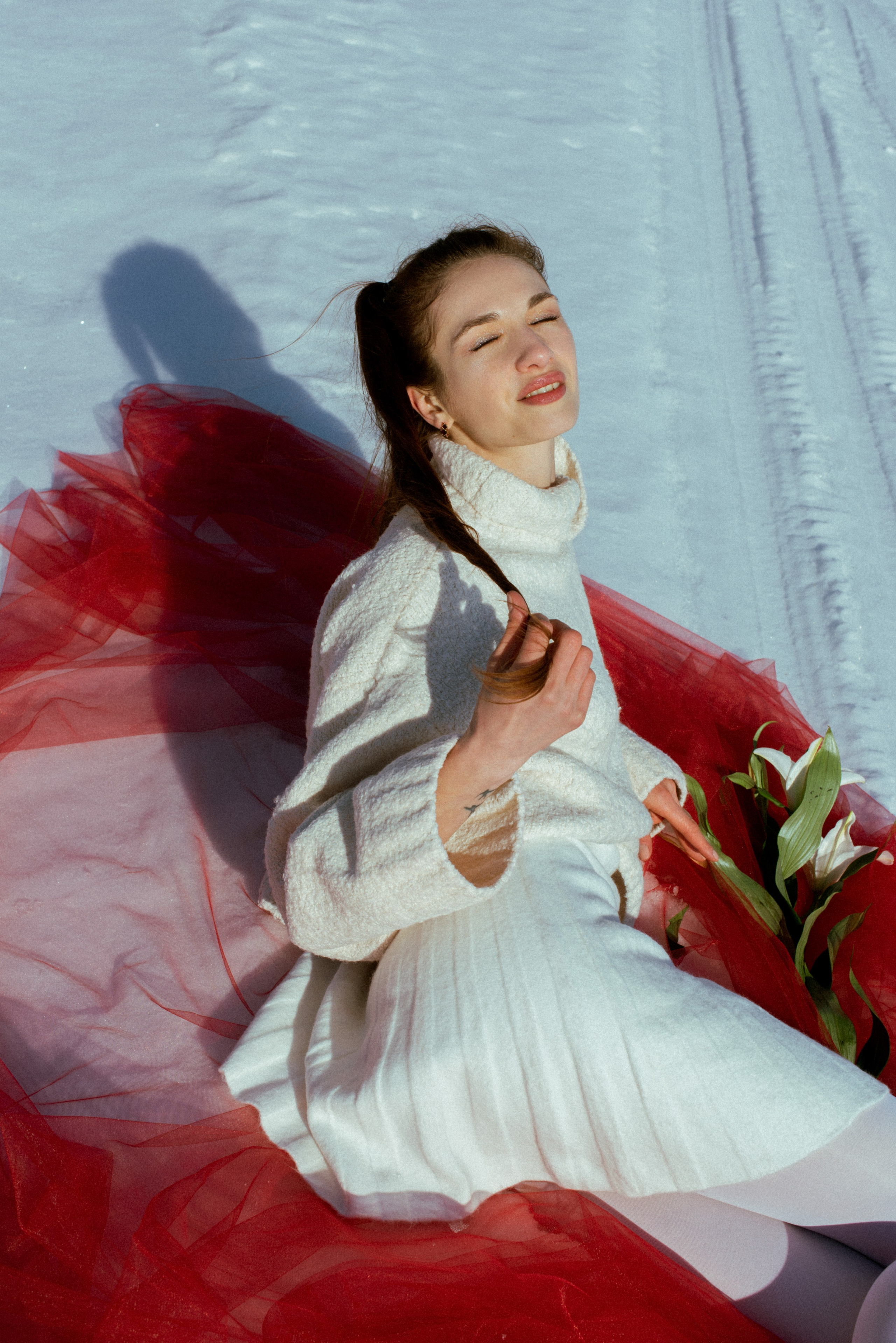 На снегу — нежный образ: Девушка в белом свитере и контрастный красный фатин.