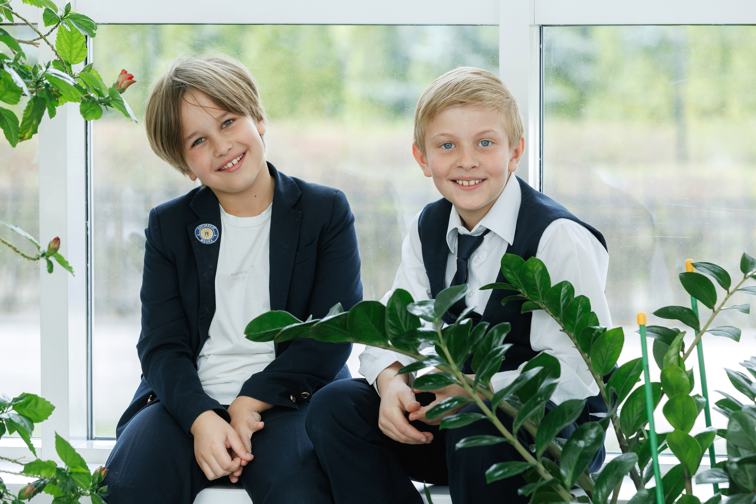 Два ученика сидят у окна среди комнатных растений