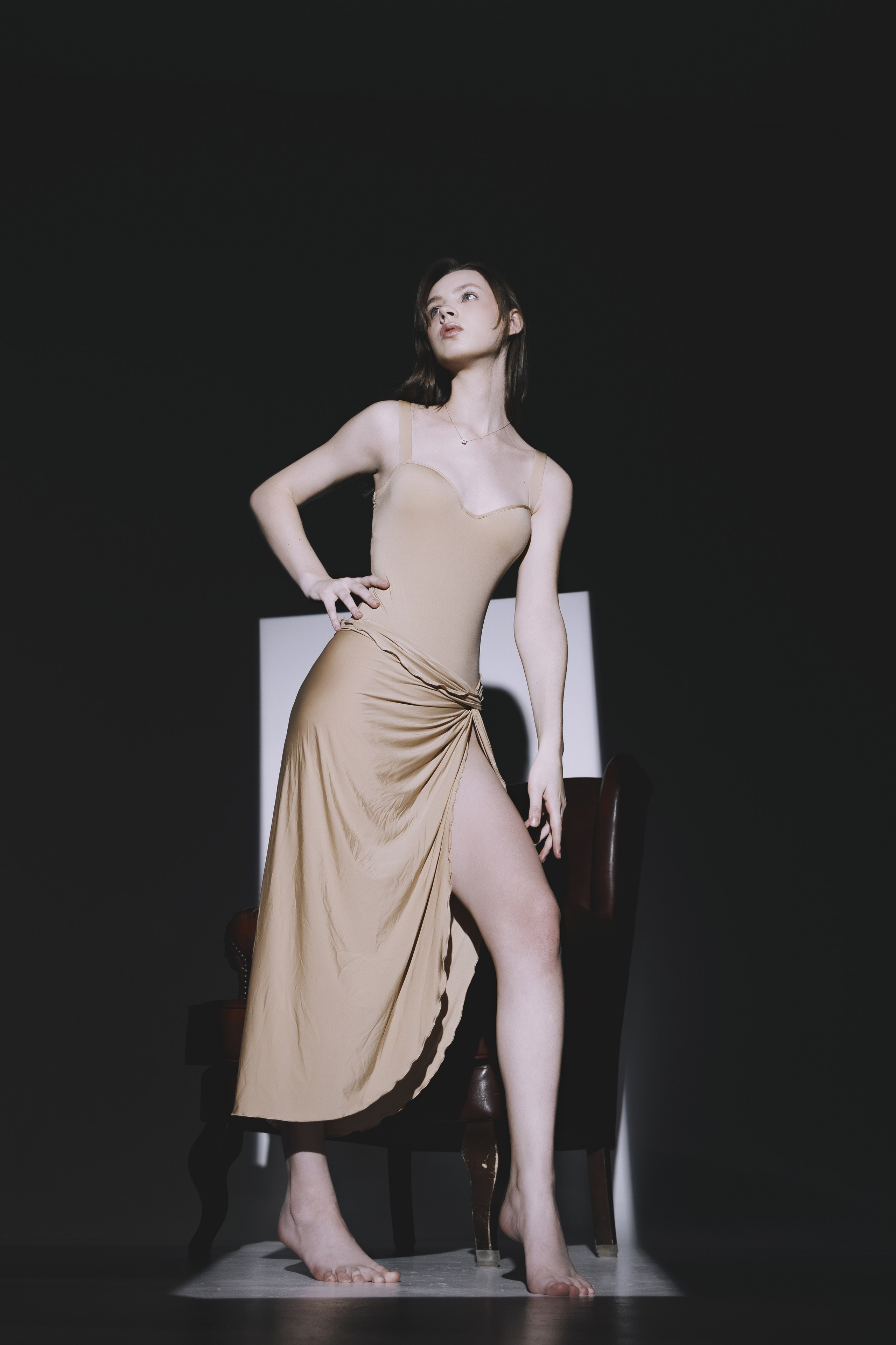 Минимализм и стиль в одной кадре: модель в облегающем платье стоит в полутени, её поза полна выразительности. Светлый прямоугольник на фоне добавляет глубины снимку.