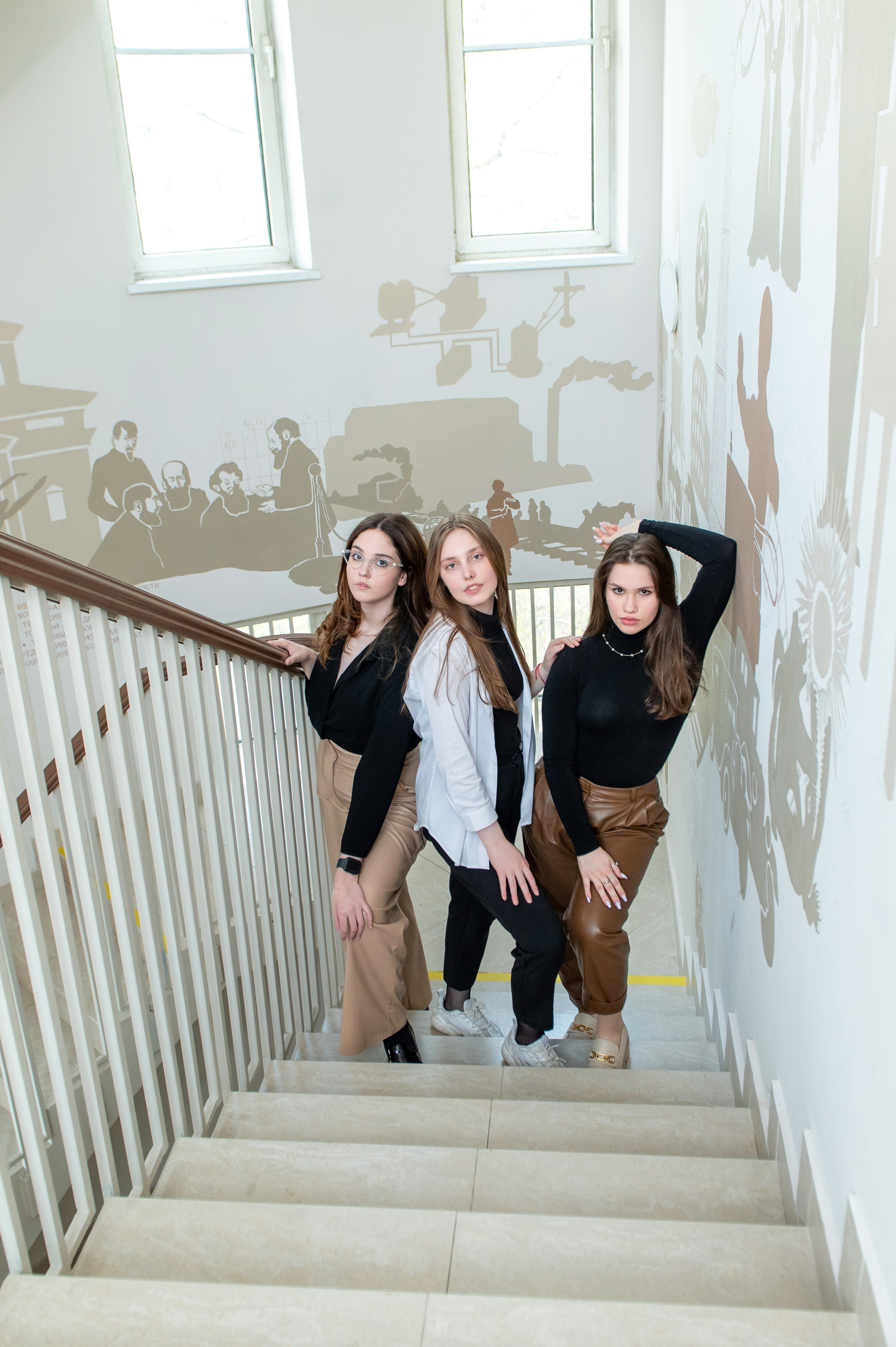 Три подруги позируют по белой лестнице.
