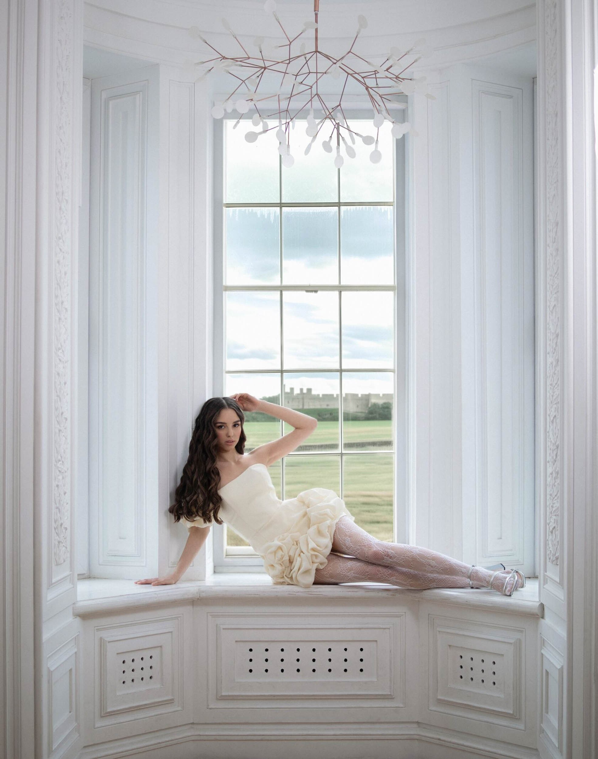 Девушка в желтом платье и белых колготках лежит на подоконнике