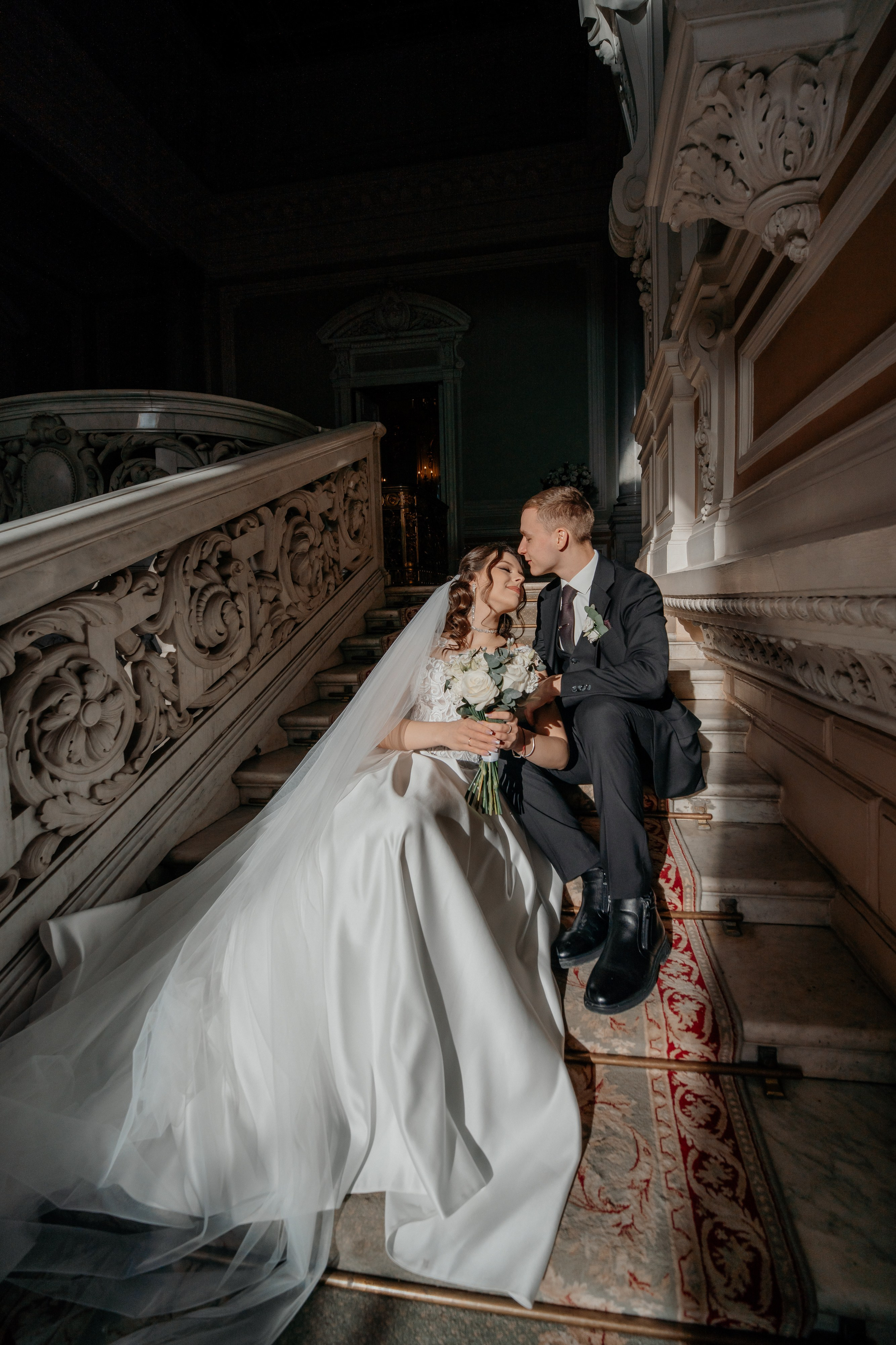 Свадебная фотосессия в Санкт-Петербурге во дворце  бракосочетания №1 на Английской набережной. Невеста и жених сидят на ступенях освещенной солнцем лестницы в лучах света.