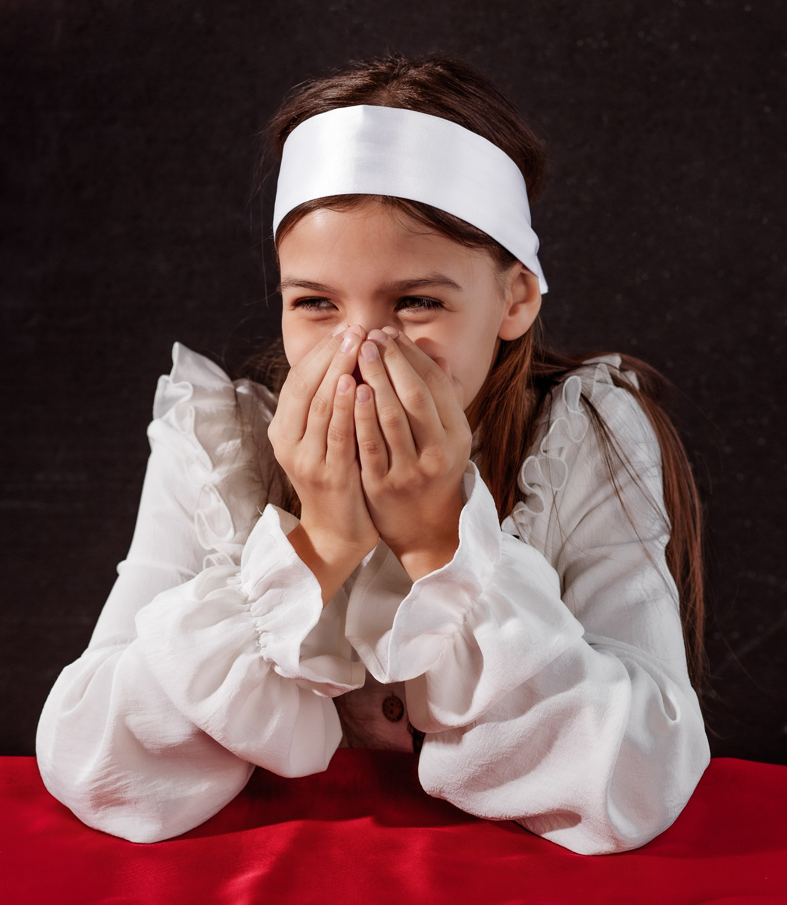 Девочка смеется закрыв рот руками.