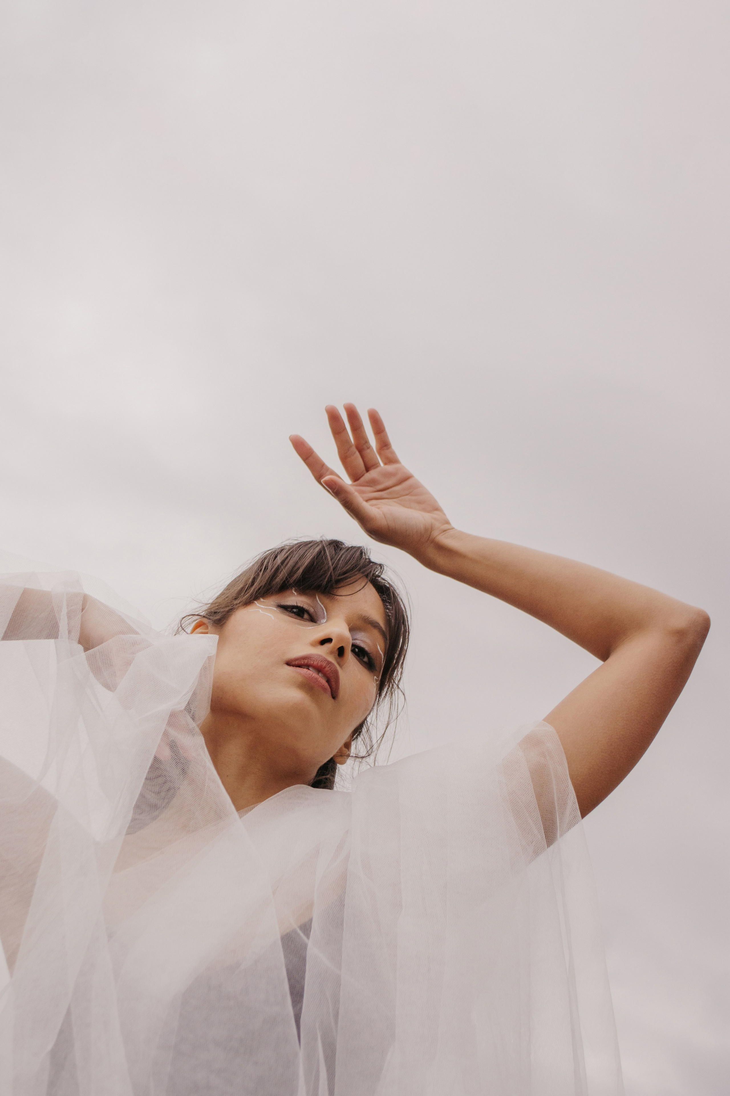Портрет балерины снизу вверх. Девушка покрыта белой тканью, она изящно поднимает руки вверх